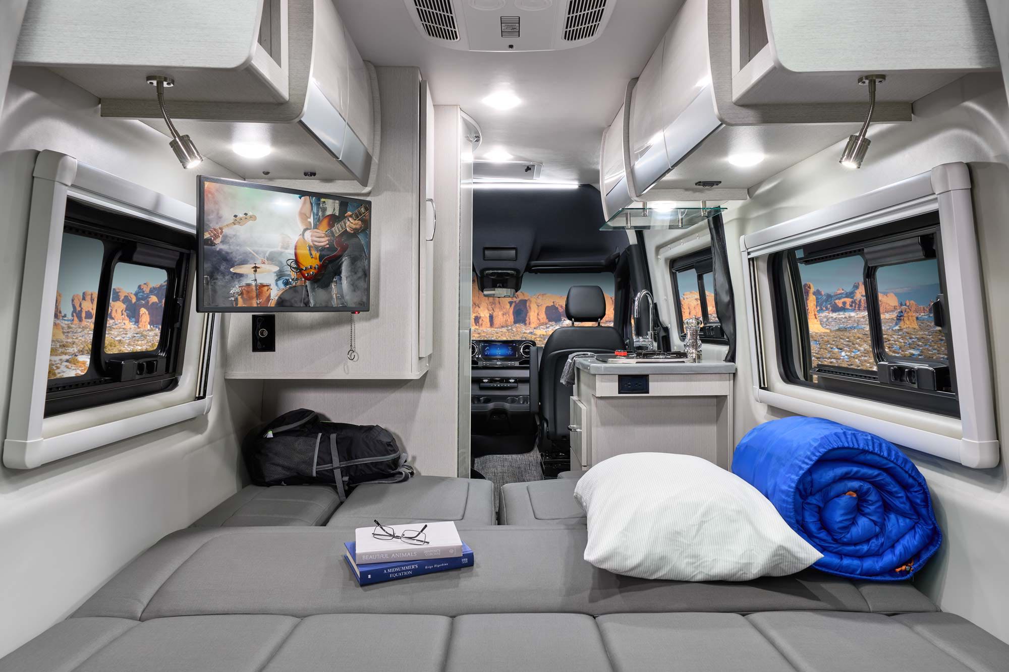 Spacious RV rental interior with a cozy bed, TV, and compact kitchen. Desert landscapes seen through the windows.. Thor Tranquility 2022