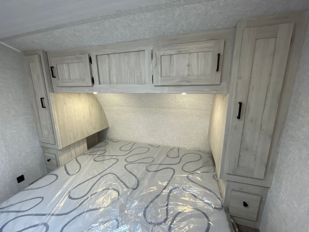 Step into this bright RV rental bedroom, featuring light-colored wood cabinets, practical overhead storage, and a protected mattress.. East to West Silver Lake 2022