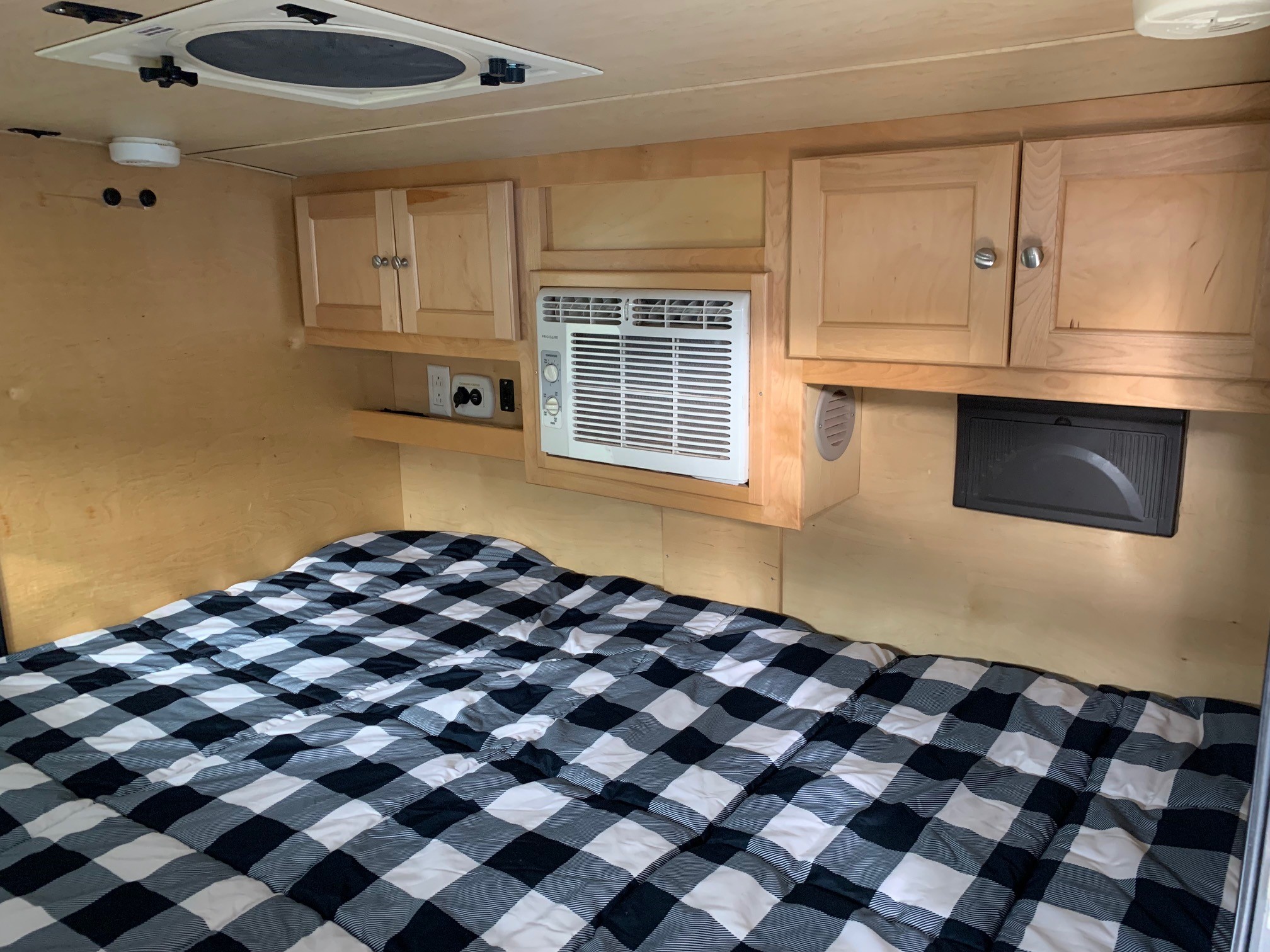 Experience this cozy RV rental bedroom. It features a bed with plaid bedding, overhead cabinets, and a convenient AC unit.. Little Guy Silver Shadow 2015