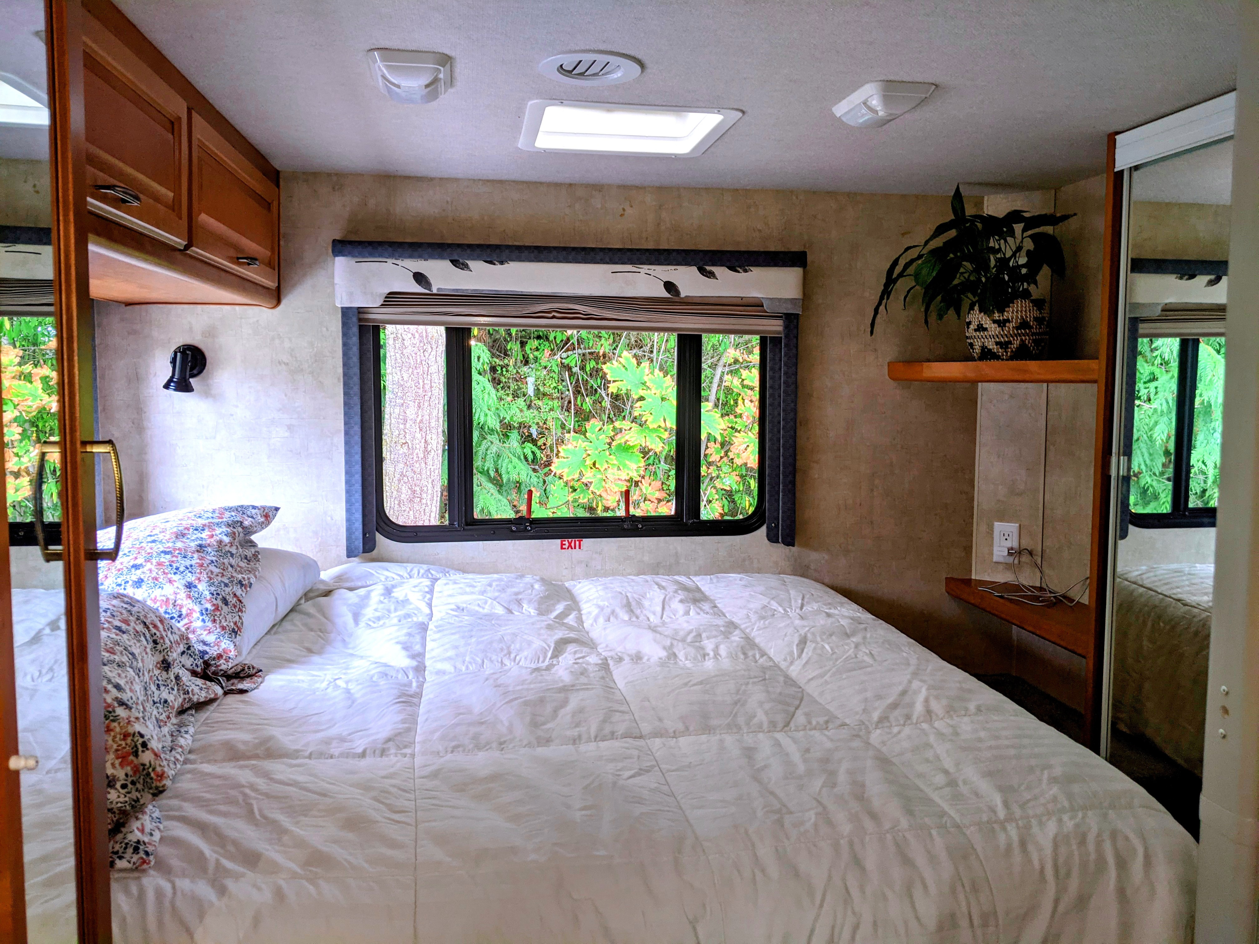 Comfortable RV rental bedroom with a large bed, nature views from the window, and convenient overhead storage/mirrored closet.. Fleetwood Tioga 2005