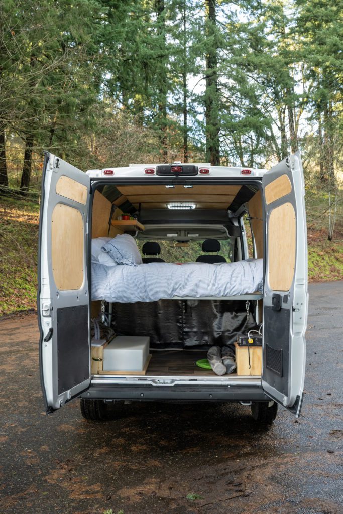 Experience van life! Rear doors open on a customized camper van interior with bed and storage, perfect for your next RV rental trip.. RAM ProMaster 2021