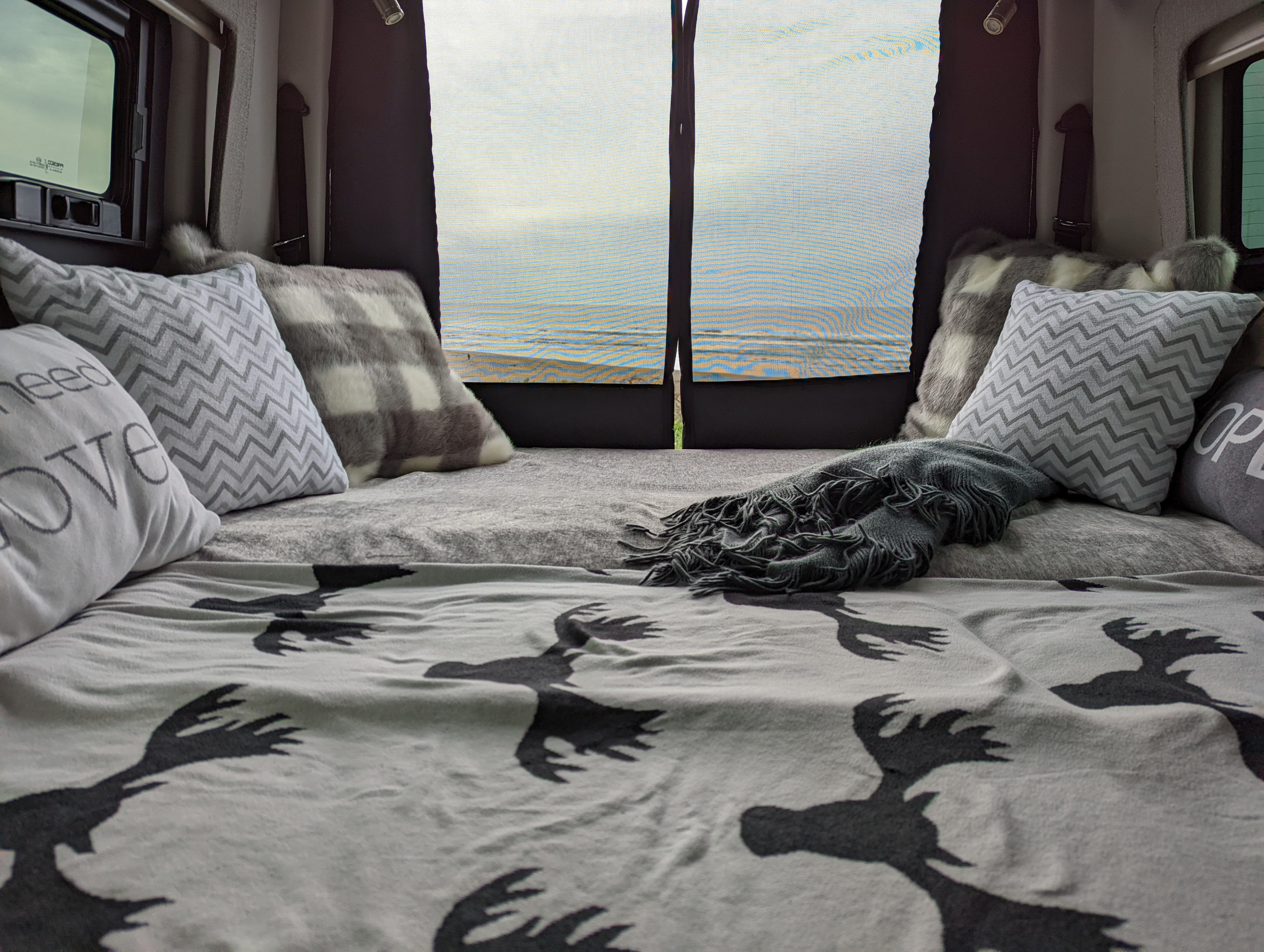 Cozy RV rental bed with patterned pillows & moose blanket, offering a beautiful beach view through the back screen.. Thor Sanctuary 2022