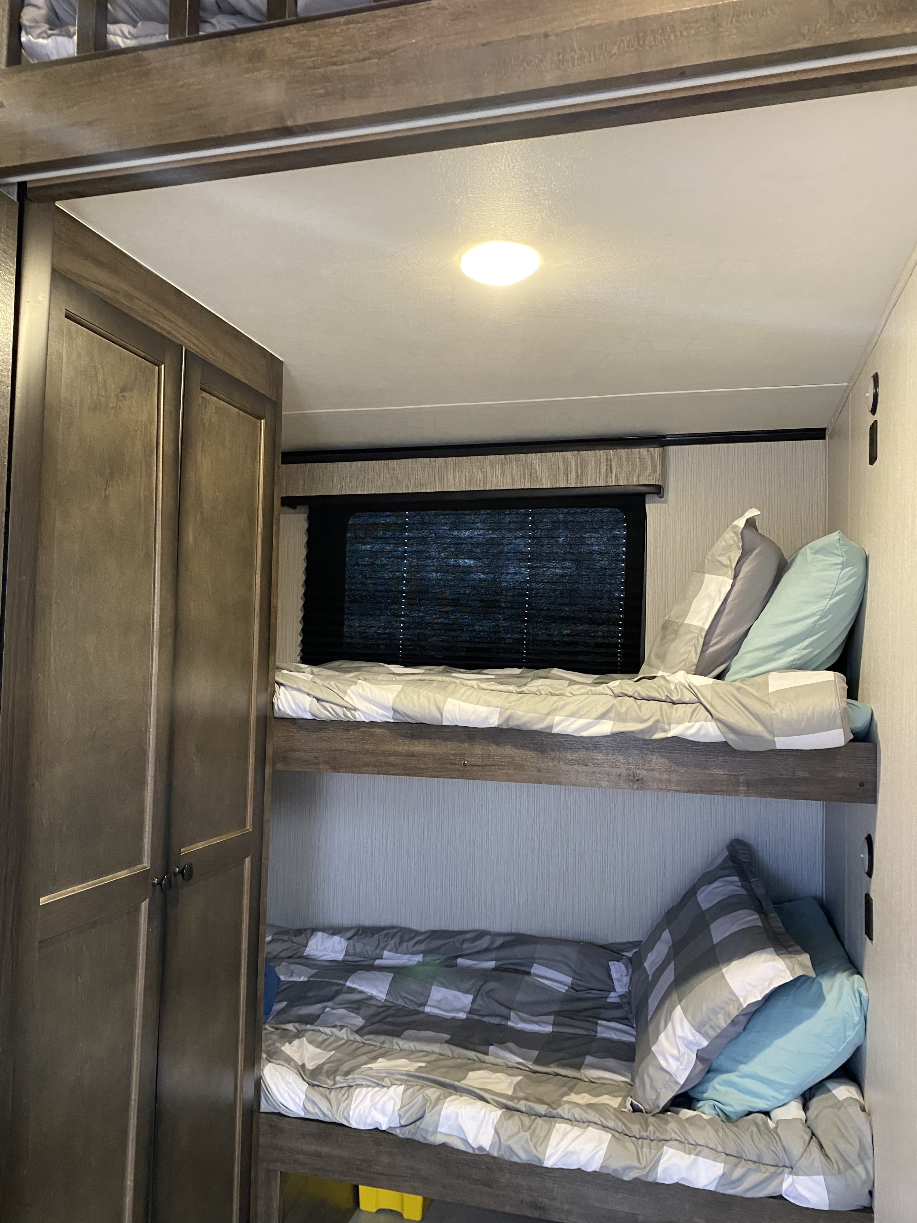 RV rental interior featuring cozy bunk beds with gray/white checkered and blue bedding, plus a dark wood cabinet on the left.. Heartland Milestone 2021