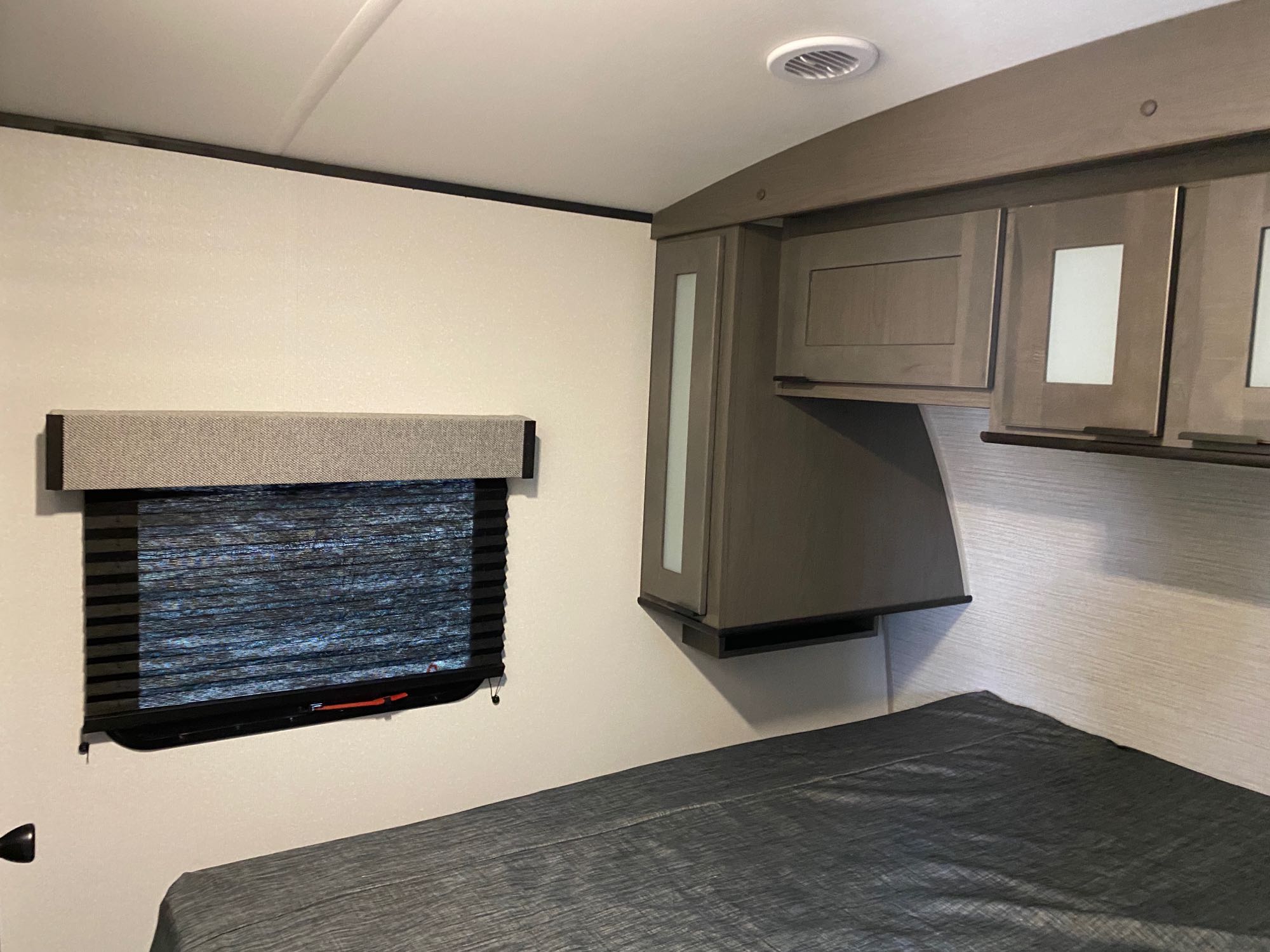 Cozy RV bedroom interior featuring a comfortable bed, window with blinds, and overhead cabinets for your RV rental.. Cruiser RV MPG Ultra Lite 2500BH 2021