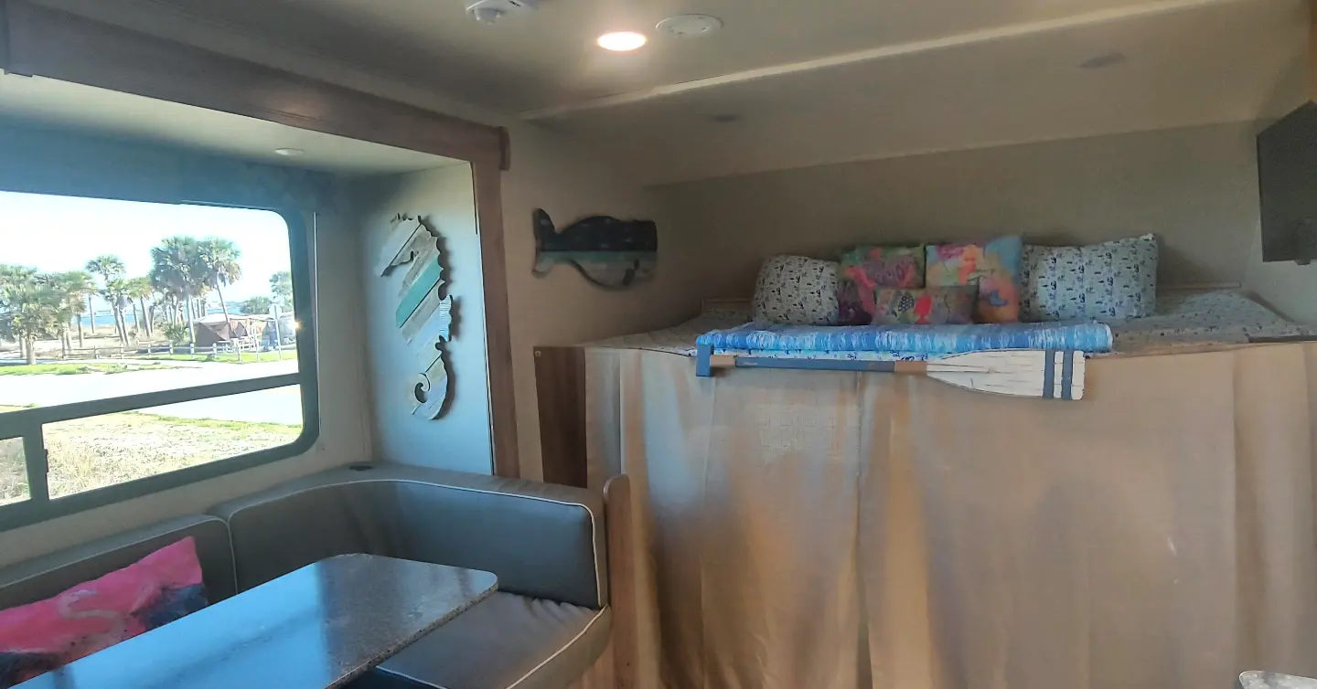 Cozy RV rental interior with coastal decor, bunk bed, and dining area. Enjoy the beach view!. Jayco Redhawk 2020
