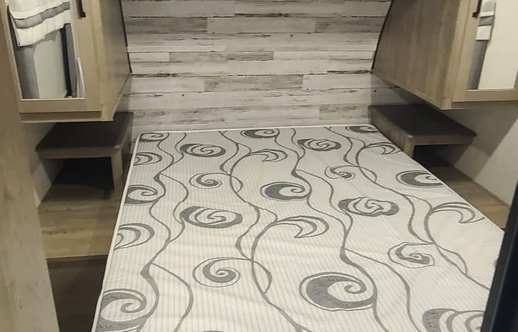 RV rental bedroom: cozy sleeping area with patterned mattress, wall paneling, overhead cabinets, and bedside tables.. Palomino Puma 28DBFQ 2021