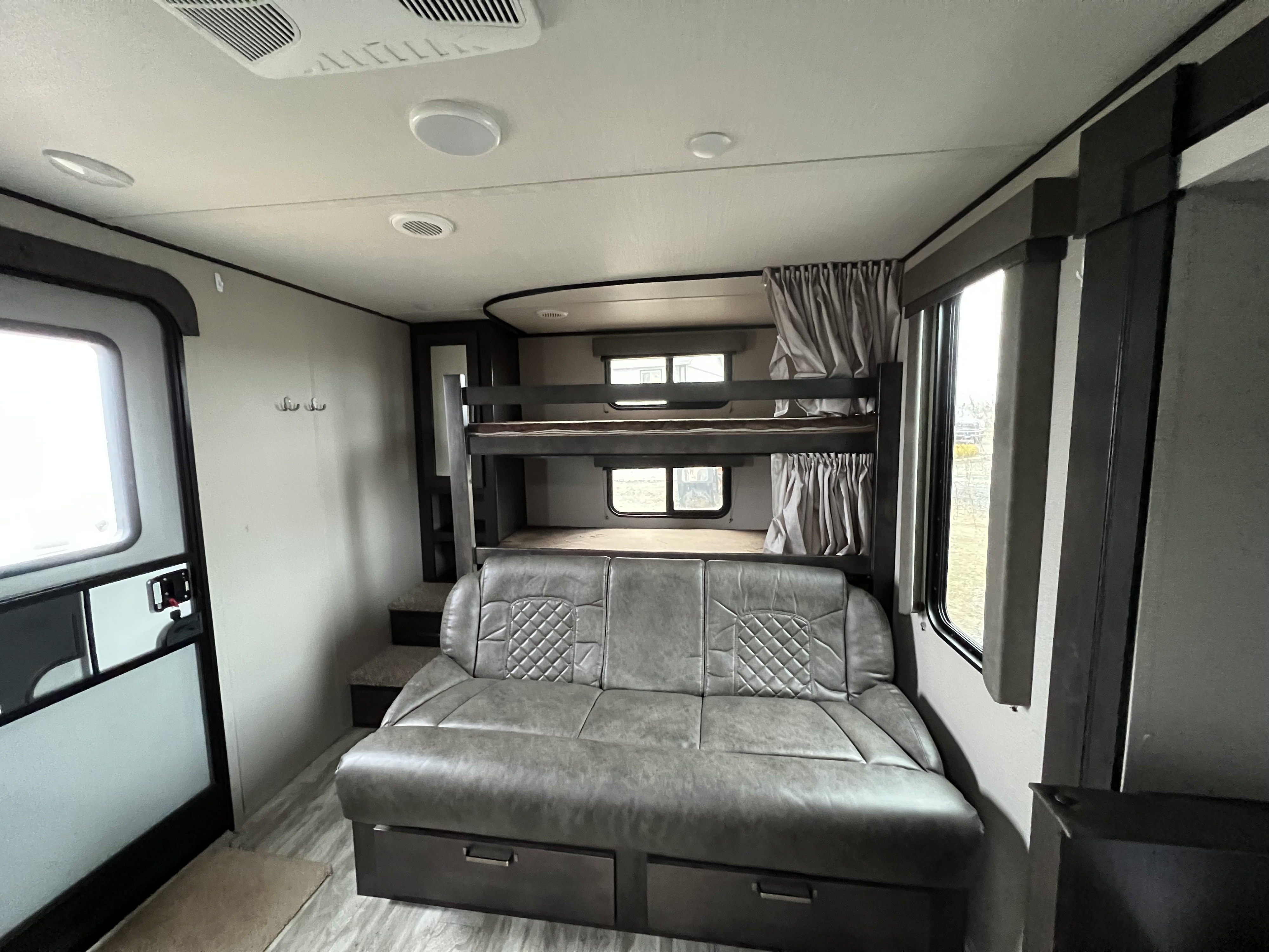 **rv rental** interior: a cozy gray sofa bed with storage, alongside bunk beds and windows, creating a family-friendly space.. Grand Design Transcend XPLOR 2020