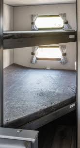 Stacked bunk beds in an RV rental. Each bunk has a window with curtains and grey bedding, offering cozy sleeping space inside a recreational vehicle.. K/Z Sportsman SE 2022