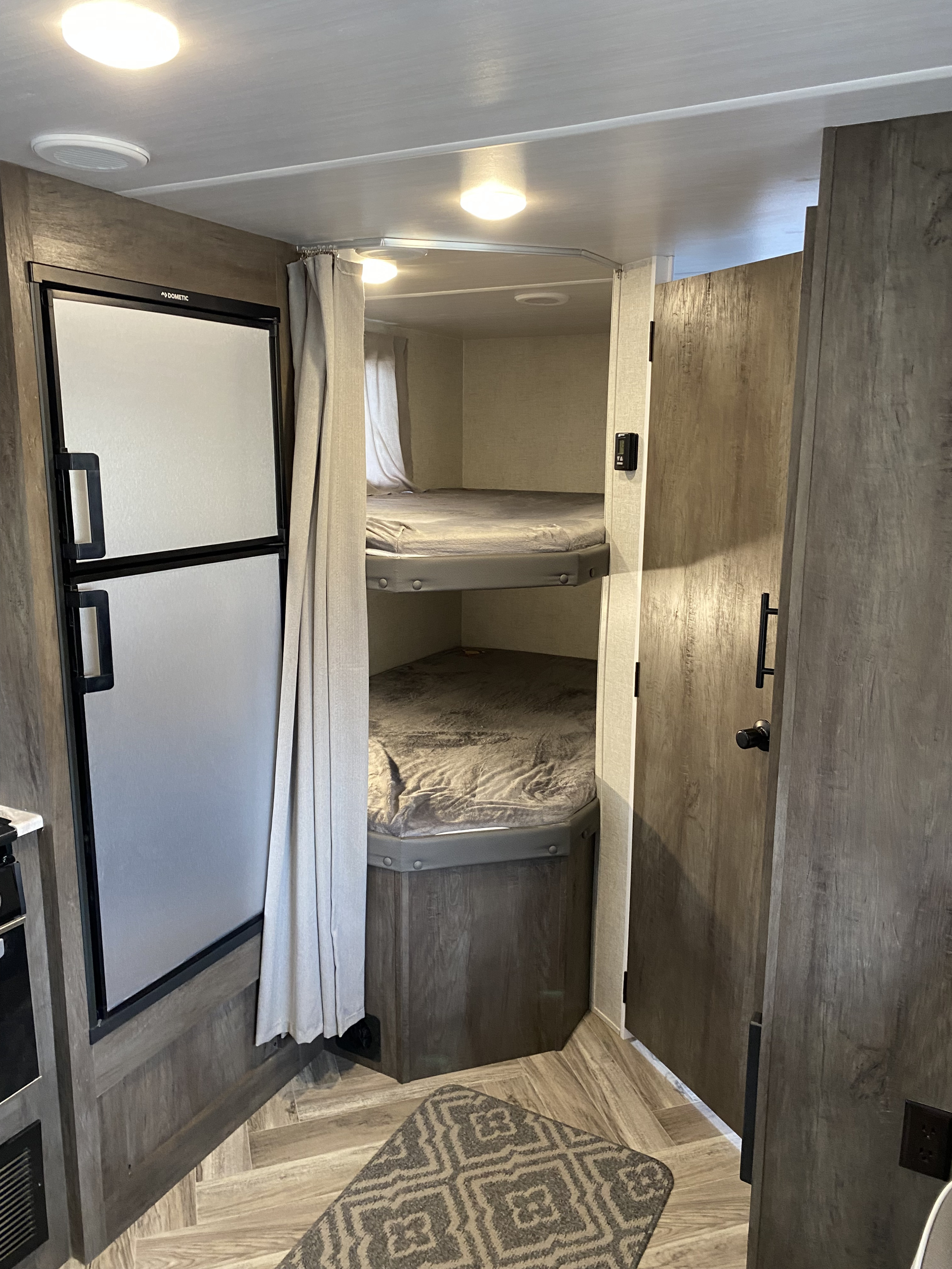 Inside an RV rental: a Dometic refrigerator stands next to curtained bunk beds, offering compact living space.. Forest River Salem Cruise Lite 2021
