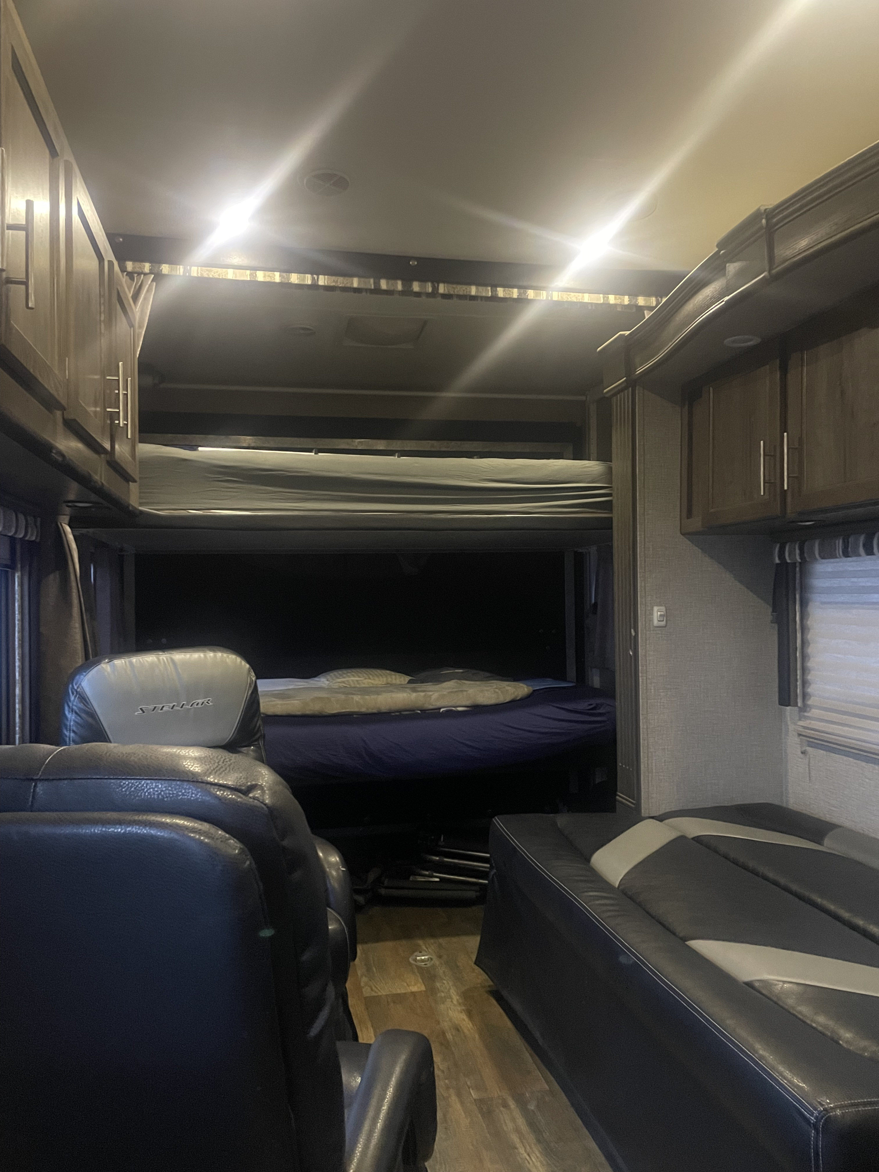 Interior of an RV rental: a large living area with a raised bunk bed, lower bed, black recliners, and wood-look cabinetry.. Eclipse Stellar Wide Lite Toy Hauler 2016