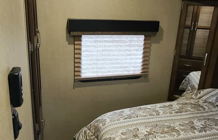 Cozy RV rental bedroom with a patterned bed, window with blinds, and wooden wardrobe for storage.. GRAND DESIGN 312BHTS 2019