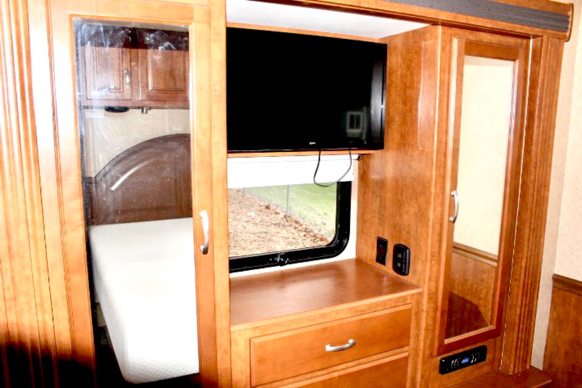 Inside an RV rental, this cozy bedroom area boasts a mounted TV, a window, and built-in mirrored storage cabinetry.. Thor Challenger 2015