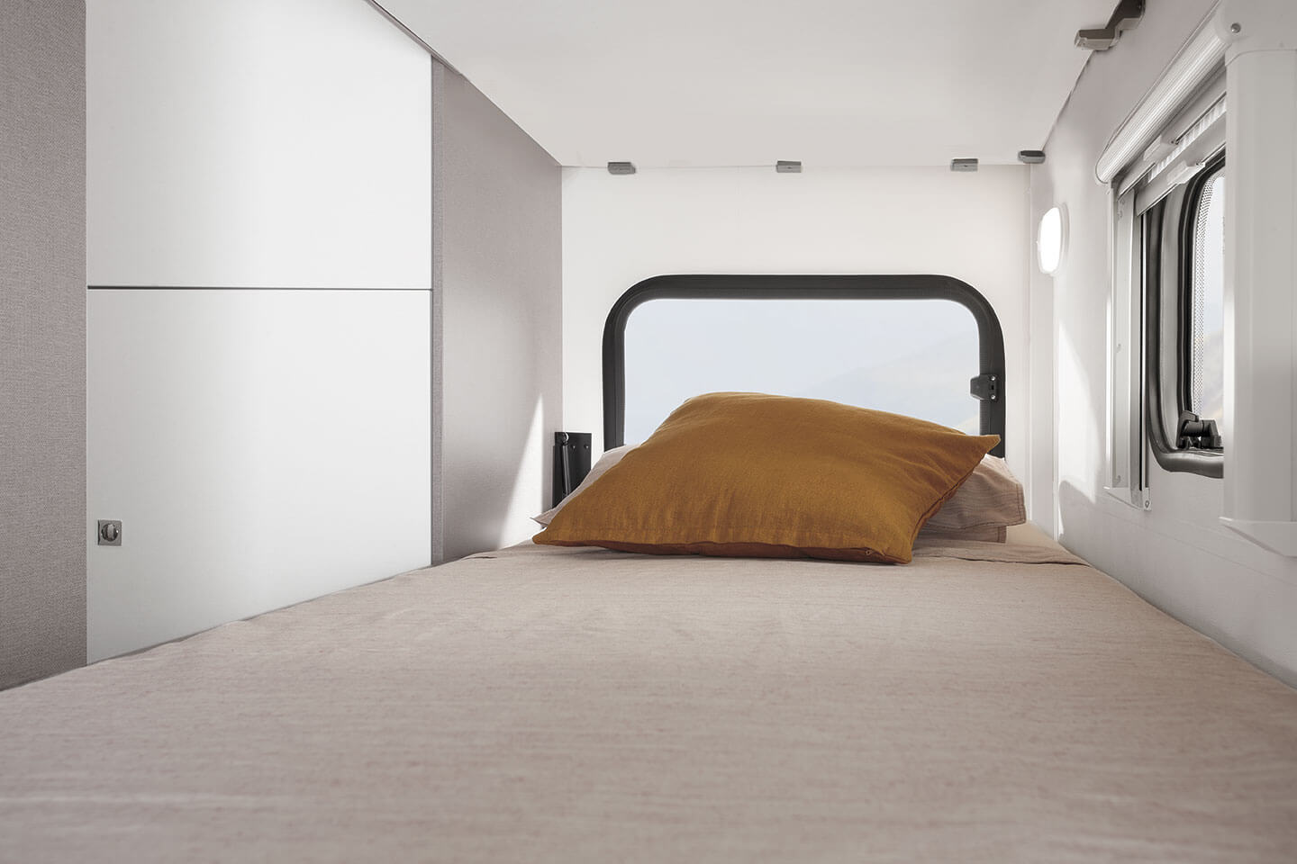 A bright, modern RV rental bedroom featuring a made bed with a yellow pillow, a large window, and white storage.. Etrusco A6600BB 2021