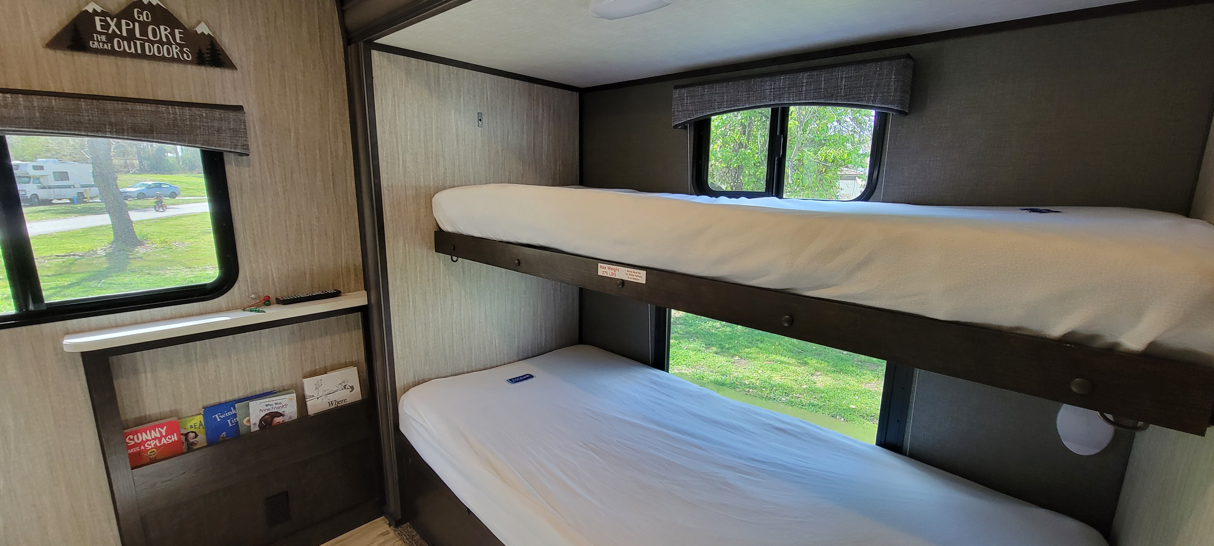 Inside an RV rental: comfy bunk beds, window views, and a 'Go Explore' sign with kids' books.. Heartland RVs Sundance 2018