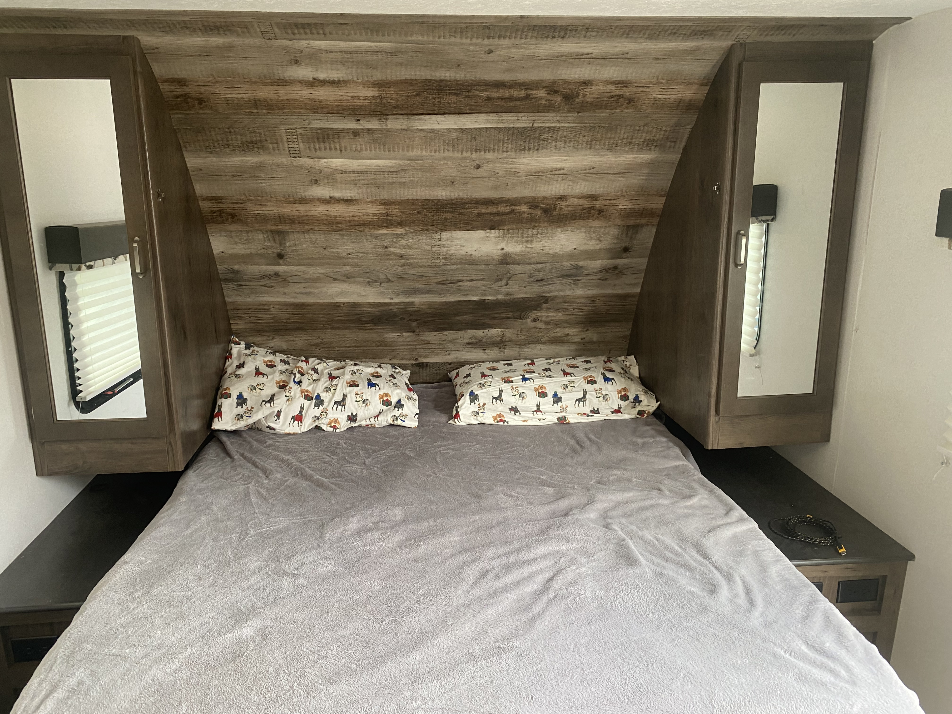 Inside an RV rental: a compact, inviting bedroom with a bed, wood headboard, and mirrored overhead storage.. Keystone Passport 2020
