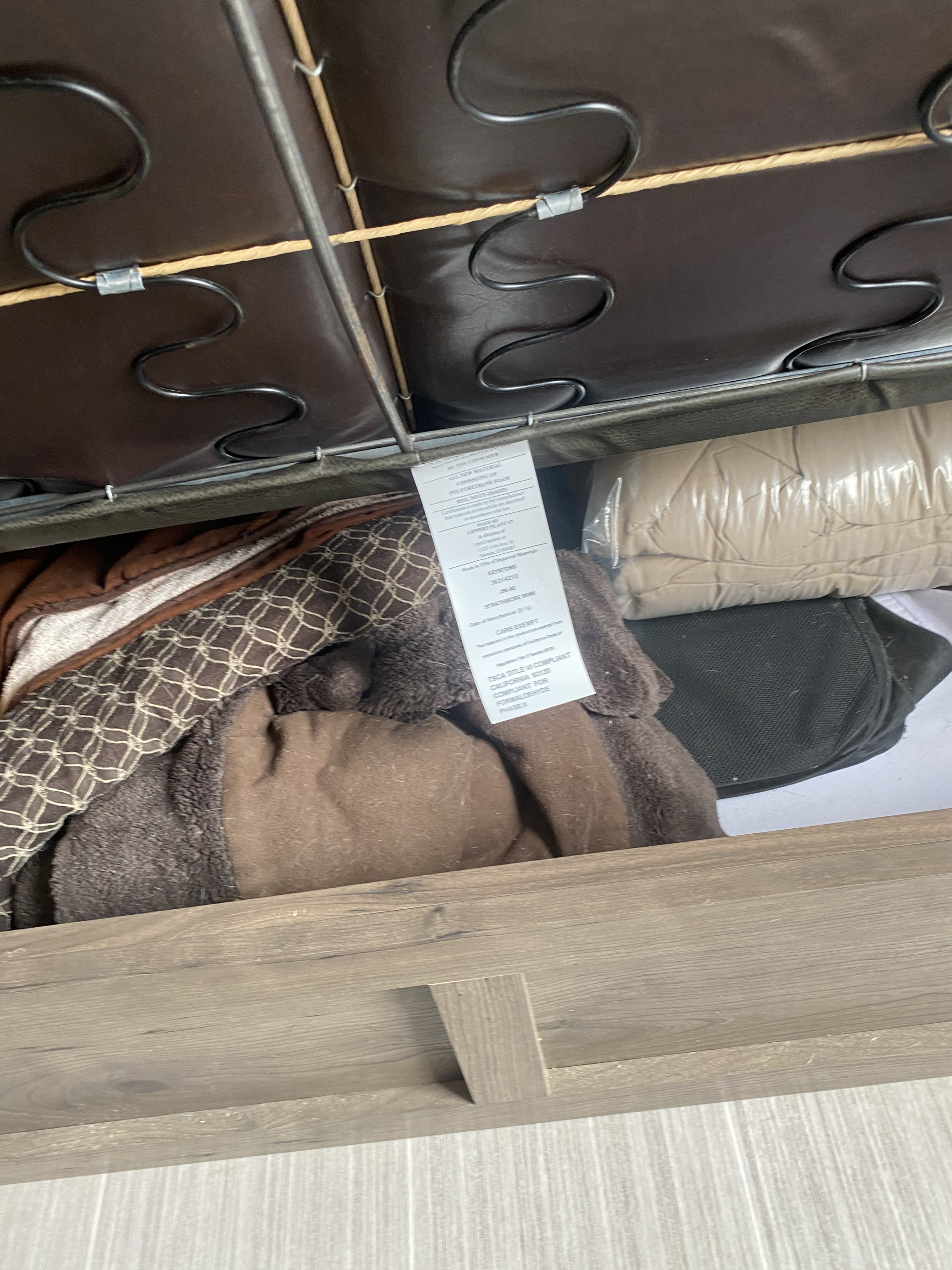 RV rental: Hidden storage under a brown sofa/bed, showing springs, a furniture tag, and packed bedding.. Keystone Passport 2020