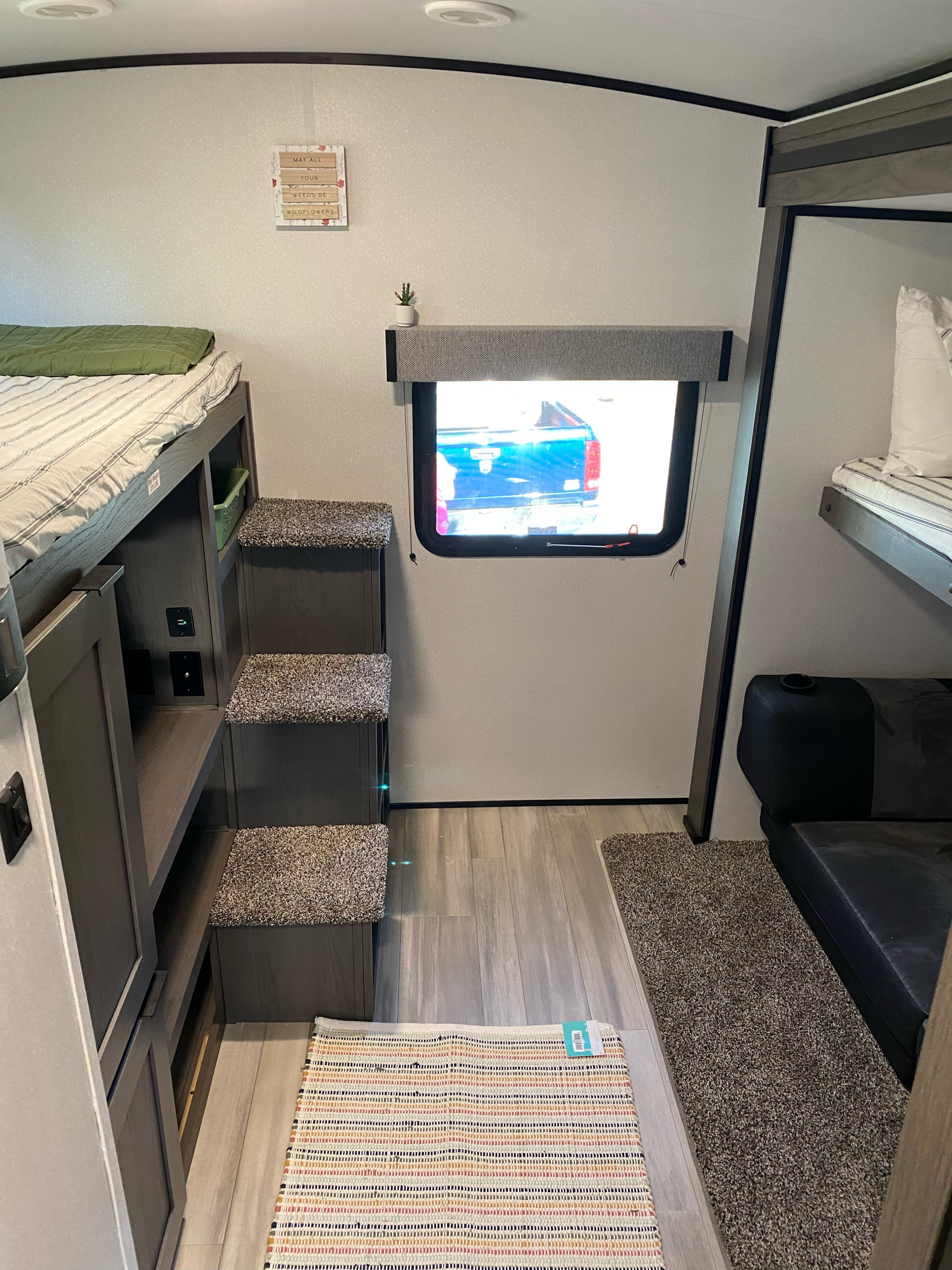 Cozy RV rental interior featuring gray bunk beds, carpeted steps, and a compact living space. A window shows a truck outside.. Cruiser RV MPG Ultra Lite 2021