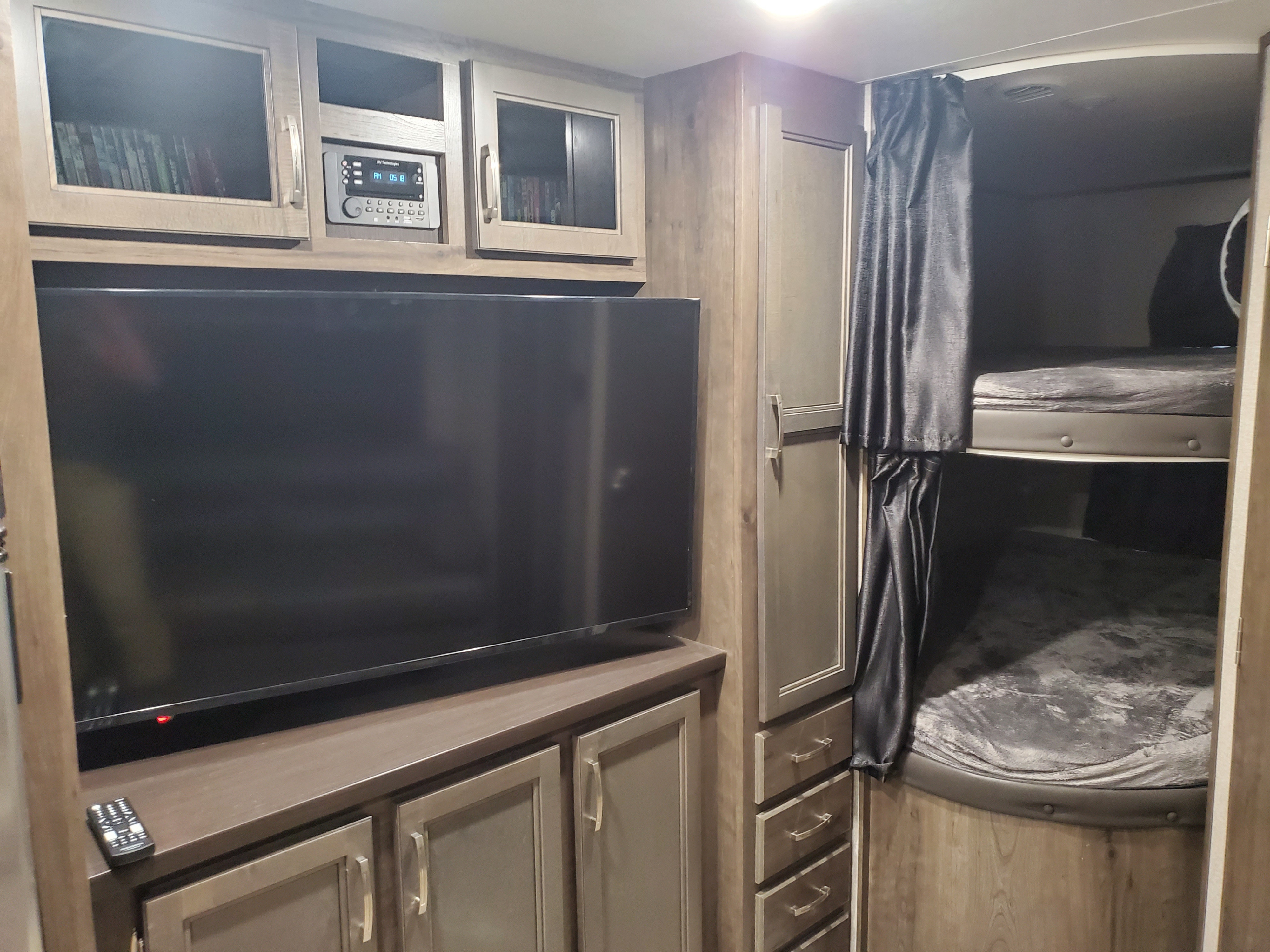 RV rental interior: cozy living space with a TV, storage cabinets, and private bunk beds with dark curtains.. Jayco Jay Flight SLX 2021