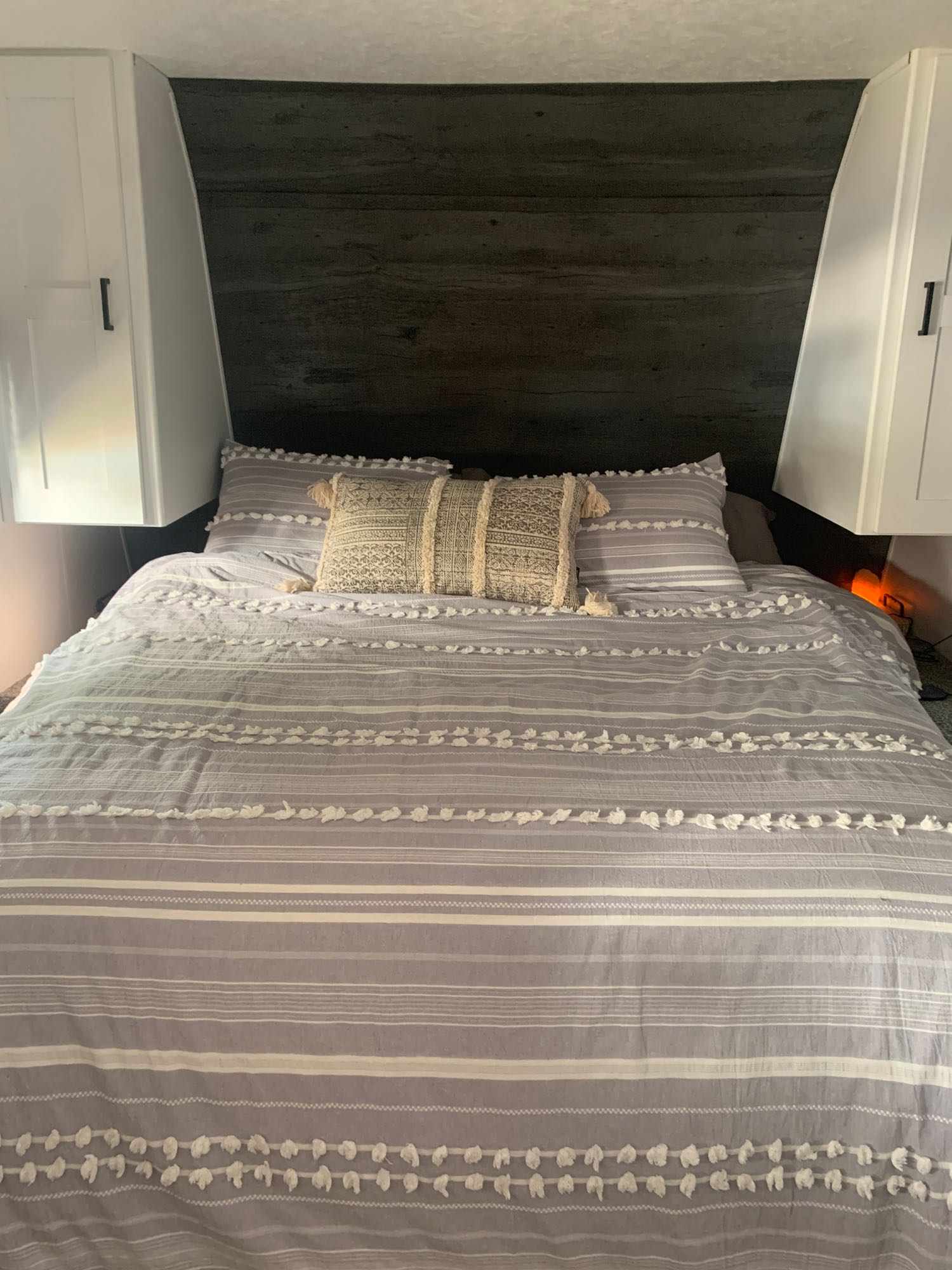 Cozy RV rental bedroom featuring a grey striped bed with textured tufts, built-in white cabinets, and a dark headboard.. Other Hideout 2021