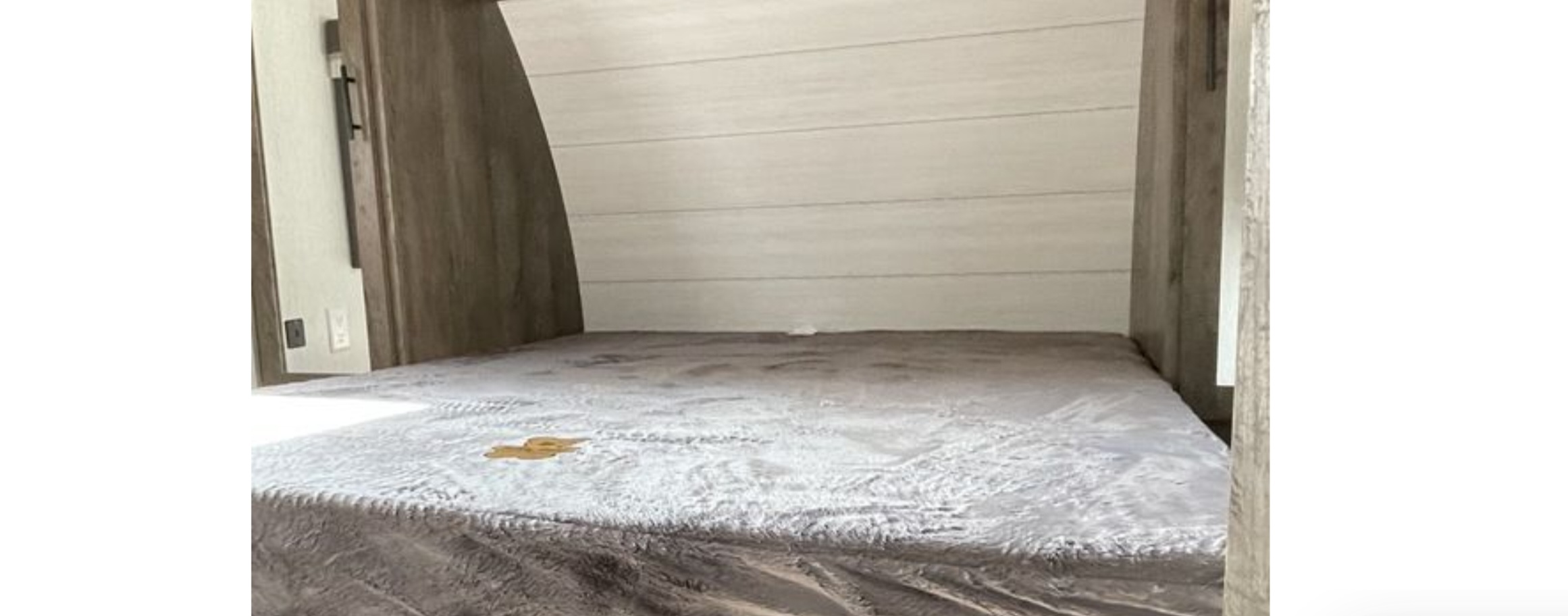 RV rental bedroom interior with a grey bed, panel headboard, and a noticeable stain on the blanket.. Forest River Wildwood X-Lite 2022