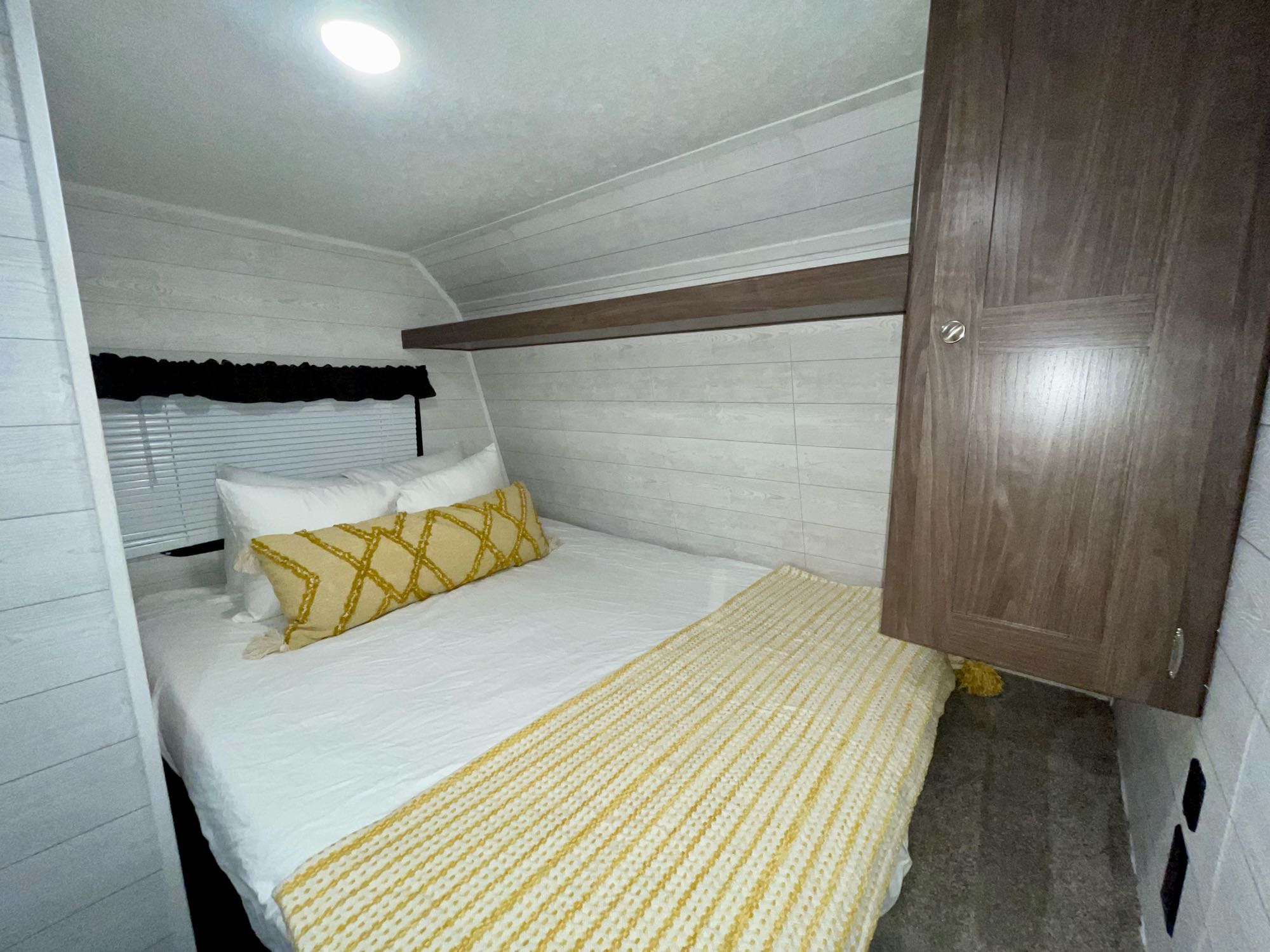 Inside a clean RV rental bedroom featuring white shiplap walls, a comfy bed with yellow accents, and storage.. Keystone Hideout 2019
