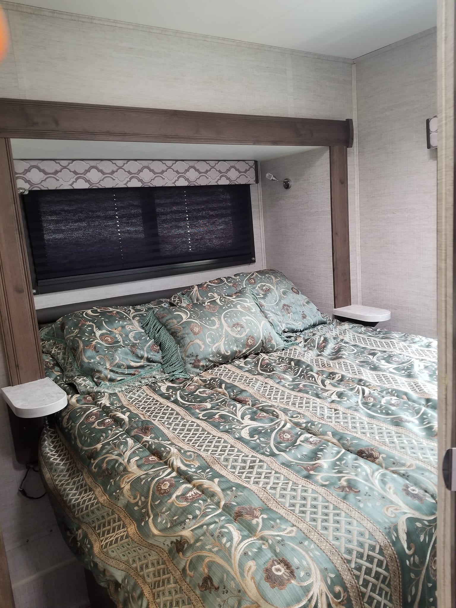 Experience comfort in this RV rental bedroom: patterned bed with floating nightstands & window shades. Compact living at its best.. Jayco Redhawk 2021