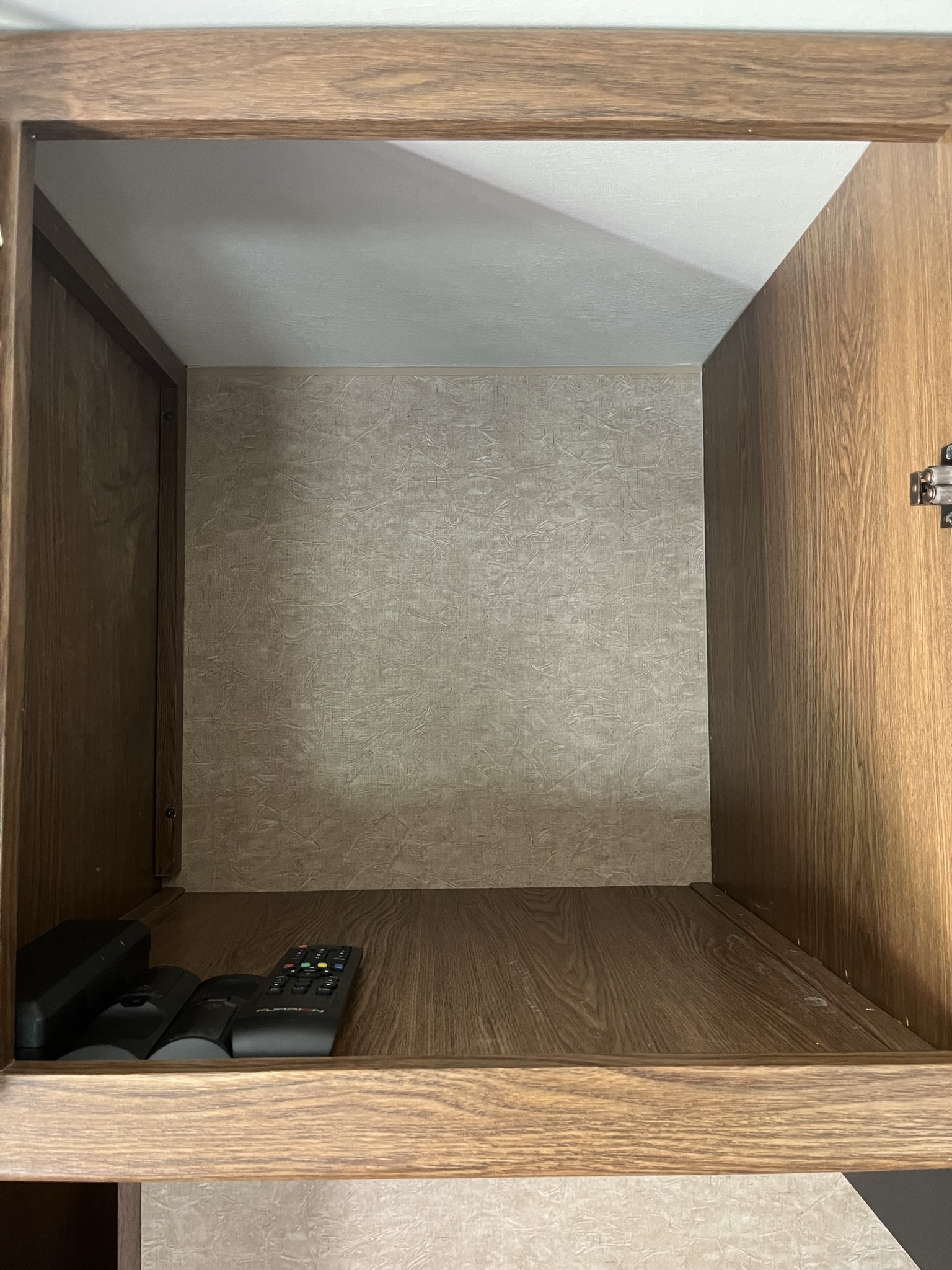 **RV rental** storage cabinet interior: an empty wooden space with three TV/device remotes on the bottom shelf.. Forest River Coachmen Leprechaun 2015