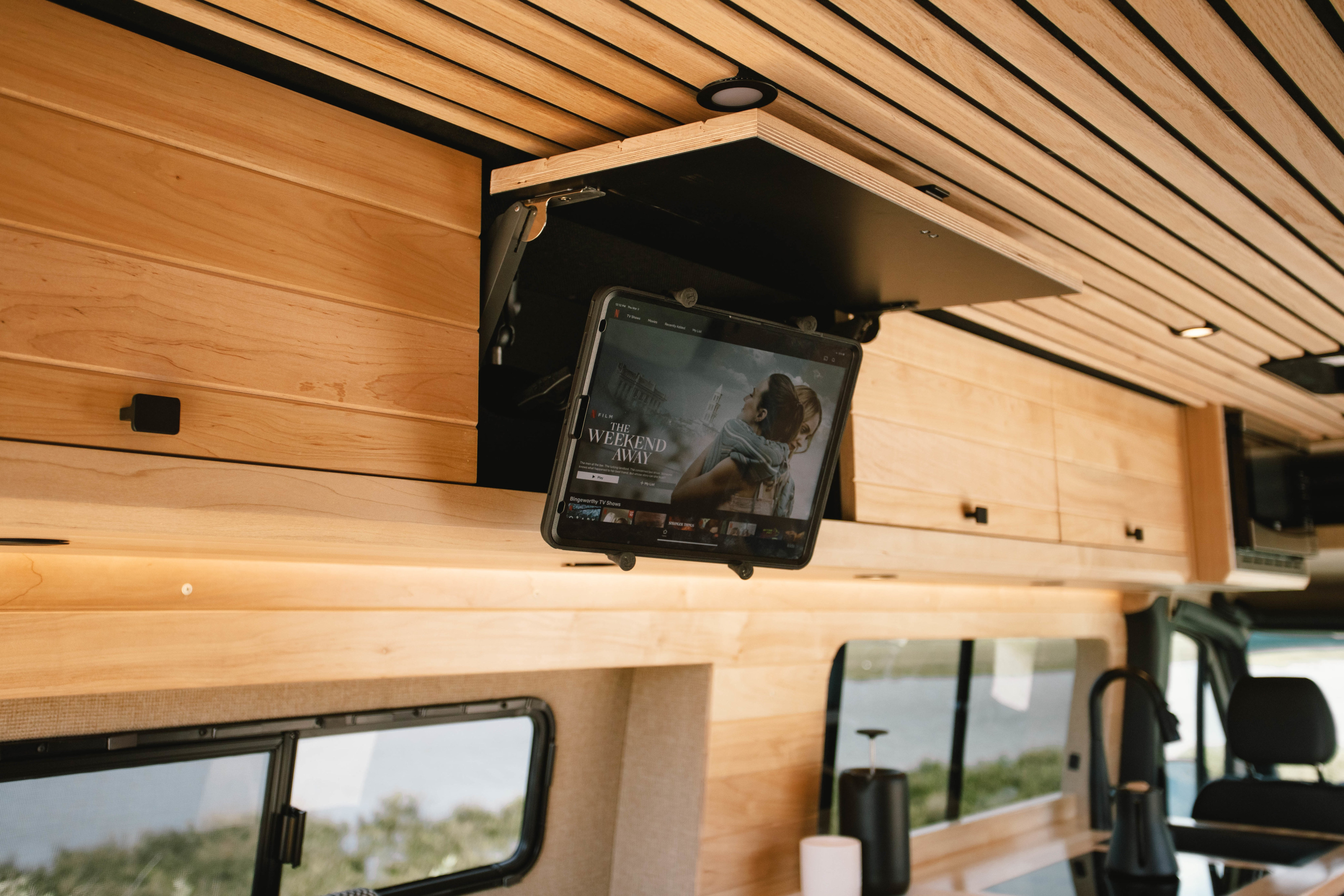 Modern RV rental interior with stylish wood paneling and a retractable tablet for entertainment, showing "The Weekend Away.". Mercedes-Benz Sprinter 2021