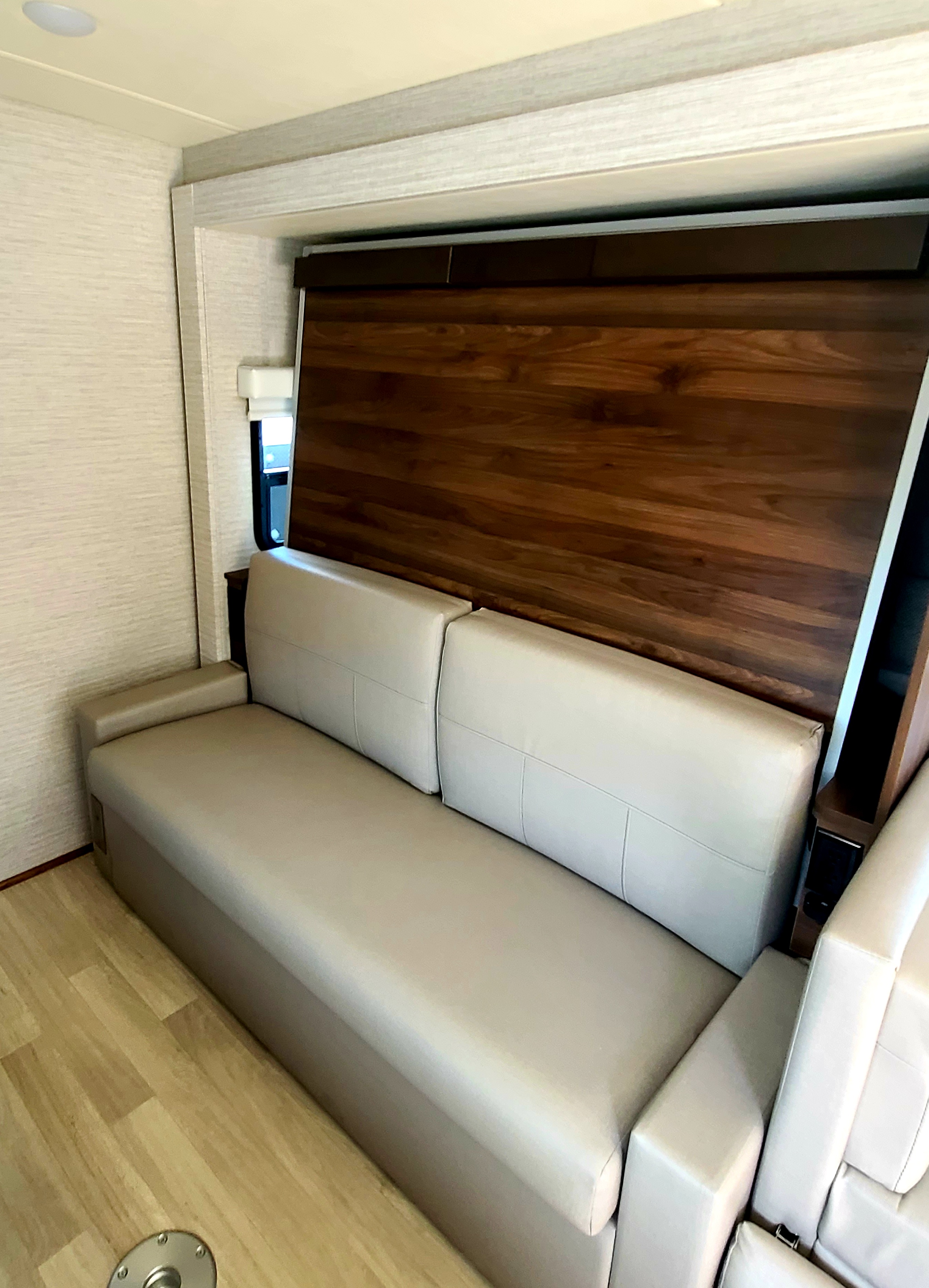 Comfortable beige sofa inside an RV rental, featuring a sleek dark wood panel, light textured walls, and wood-look flooring.. Winnebago Navion 2020