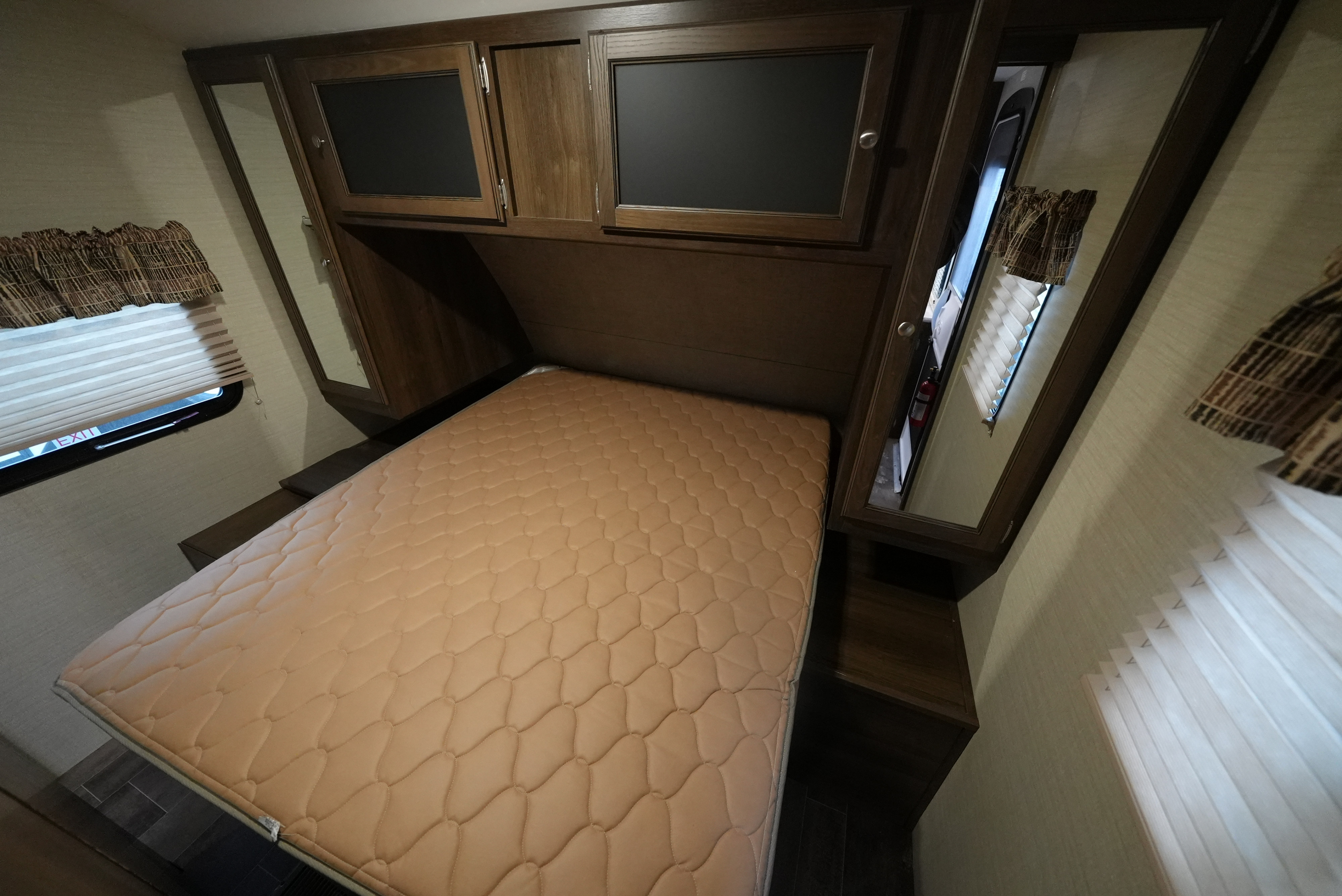 Compact RV rental bedroom featuring a quilted bed, overhead cabinets, and side windows with blinds for comfort and safety.. Keystone Bullet 2018