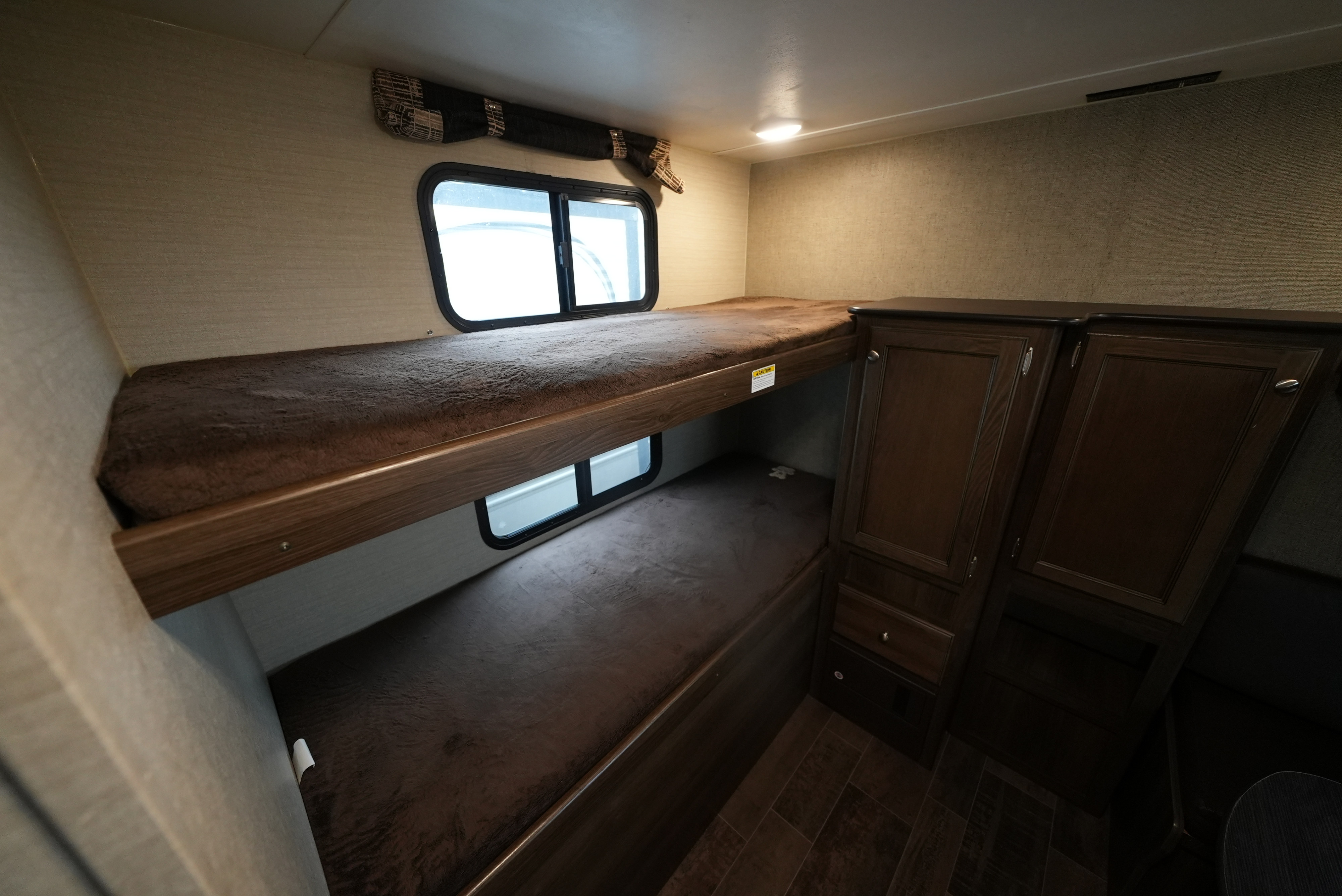 Cozy bunk beds in an **RV rental**, featuring plush brown blankets, built-in windows, and dark wood storage cabinetry.. Keystone Bullet 2018