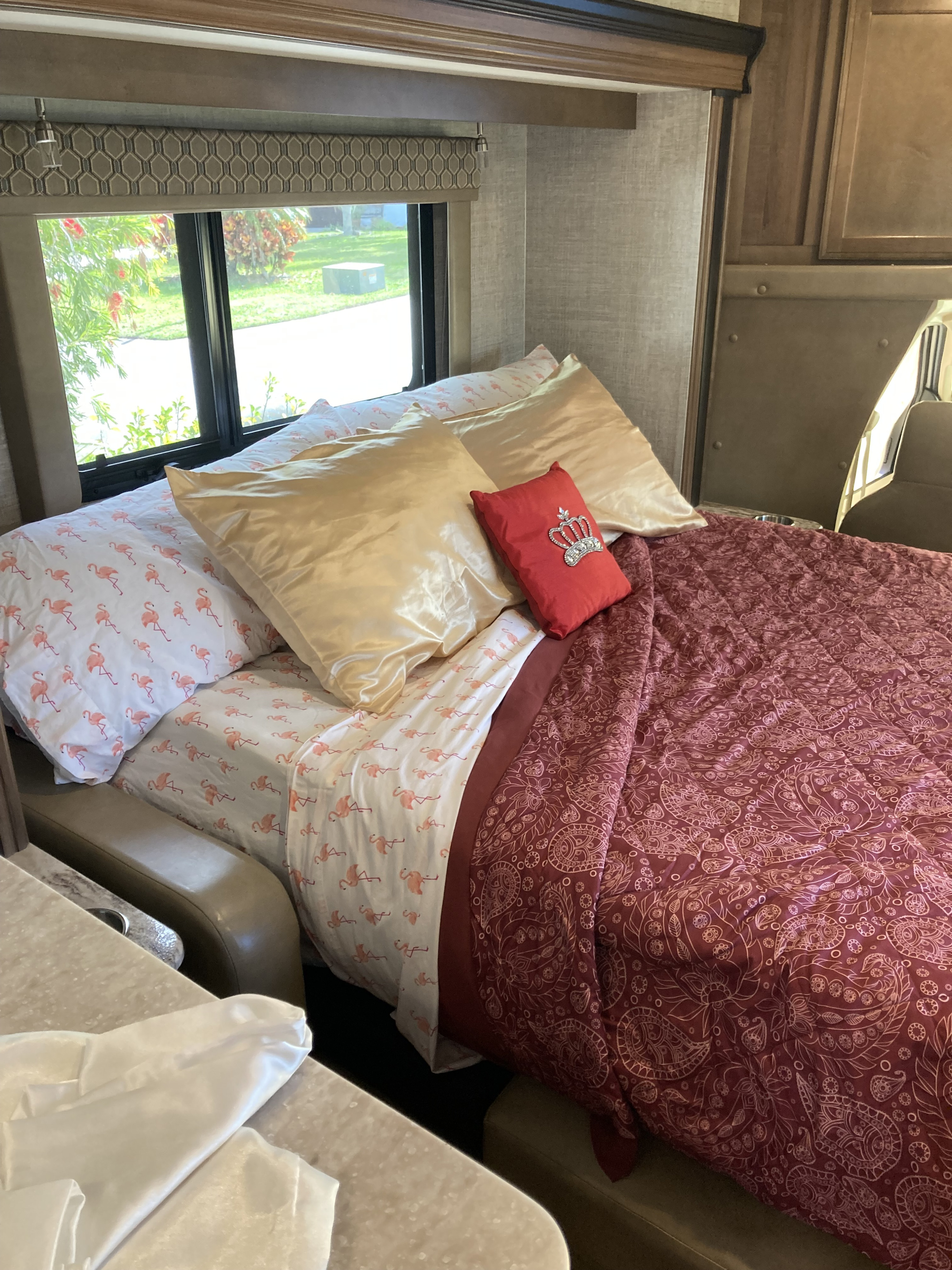 Cozy RV rental bedroom with flamingo sheets, golden pillows, and a red comforter. Ready for comfortable travel!. Gulf Stream B Touring Cruiser 2019