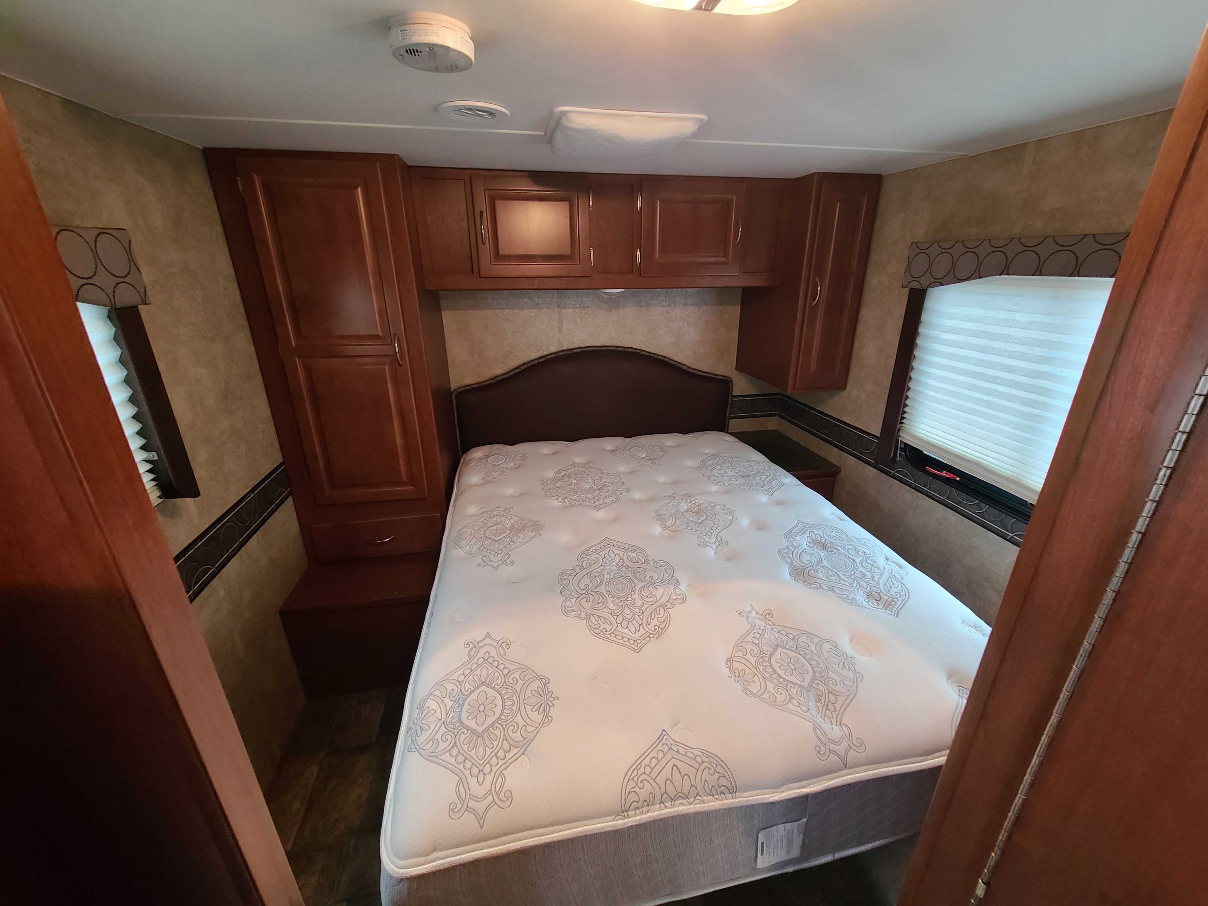 Inside this RV rental, a cozy bedroom with a comfortable bed, surrounding wooden cabinets, and a window with blinds.. Winnebago Minnie Winnie 2014