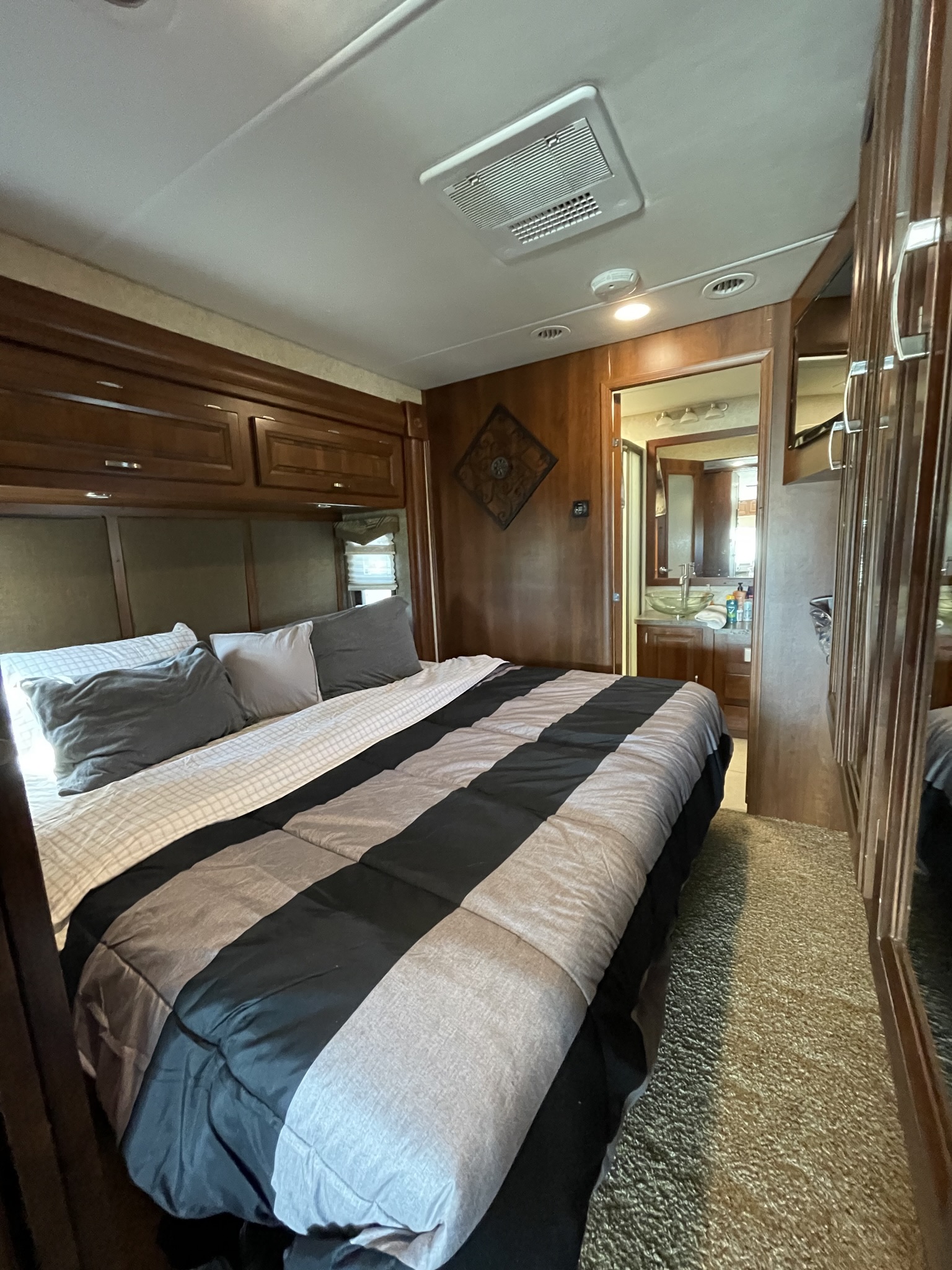 Spacious RV rental bedroom with a cozy bed and private bath. Dark wood finishes, AC, and carpeted floor create a comfortable mobile home.. Georgetown XL 2014