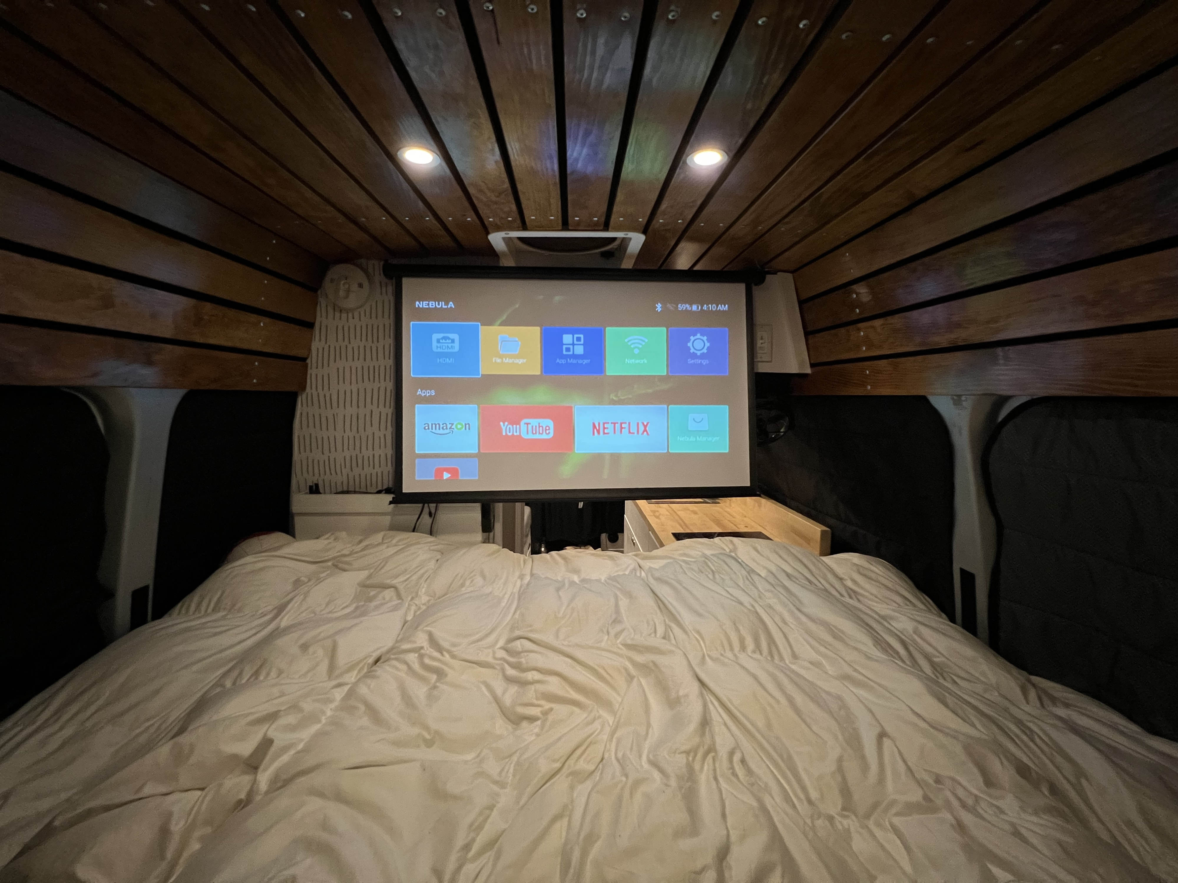 Cozy RV rental interior featuring a projector screen above the bed, displaying Netflix and other smart TV apps.. Mercedes-Benz Sprinter 2014