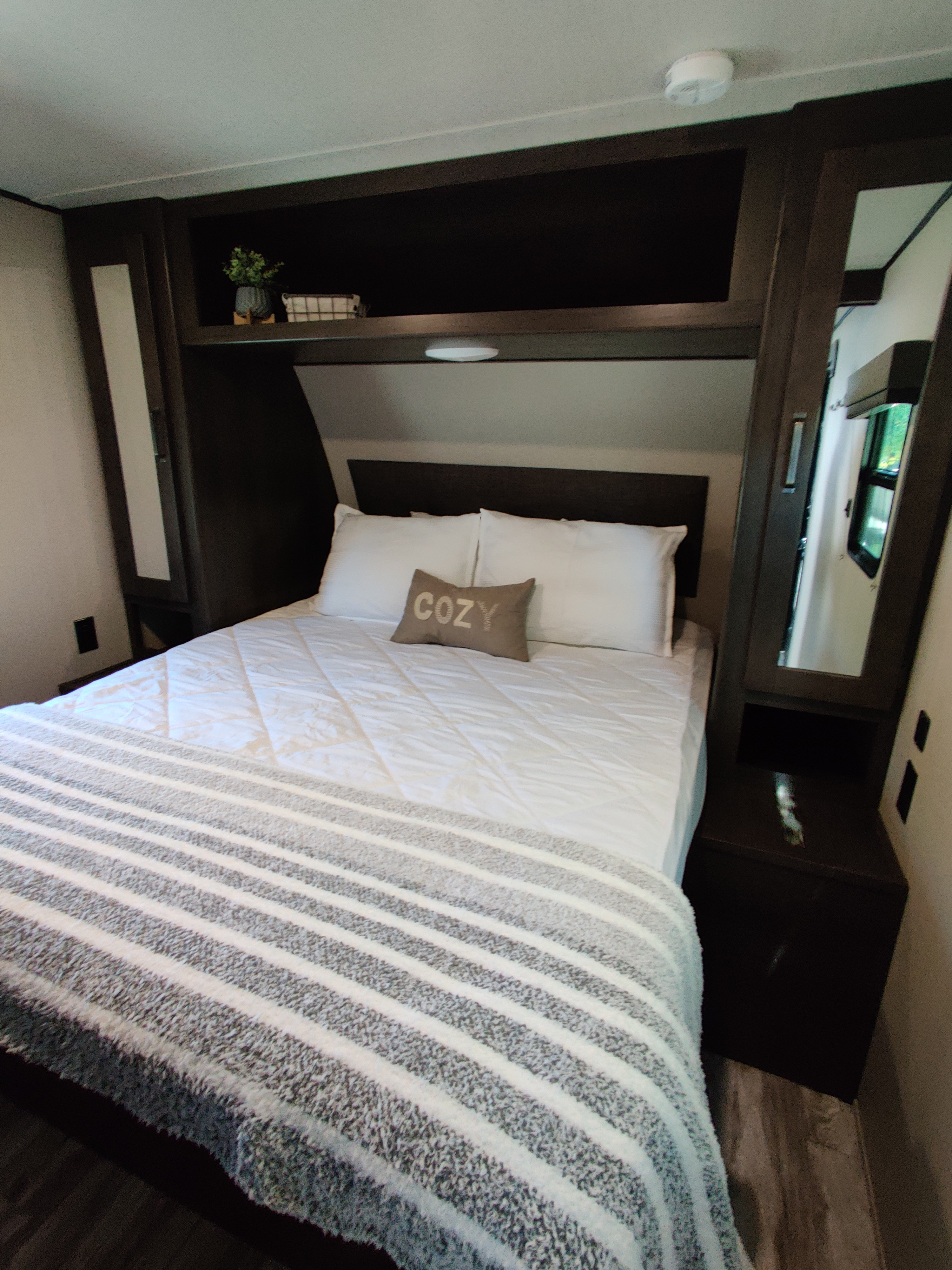 Cozy RV rental bedroom featuring a comfortable bed with white bedding, a striped blanket, and built-in storage.. Grand Design 261BH 2022
