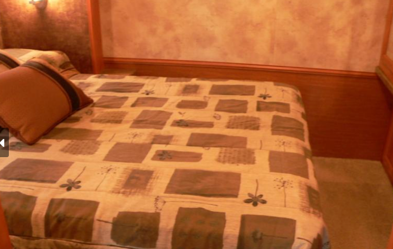 Cozy RV rental bedroom featuring a patterned comforter, brown throw pillow, and warm wood-paneled walls.. Other Other 2010