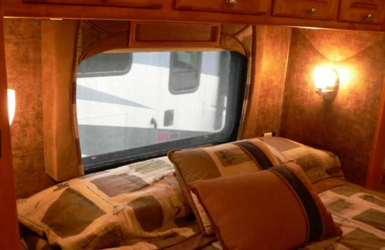 Inside a cozy RV rental bedroom: patterned bed, window view of another RV, and warm wall light.. Other Other 2010
