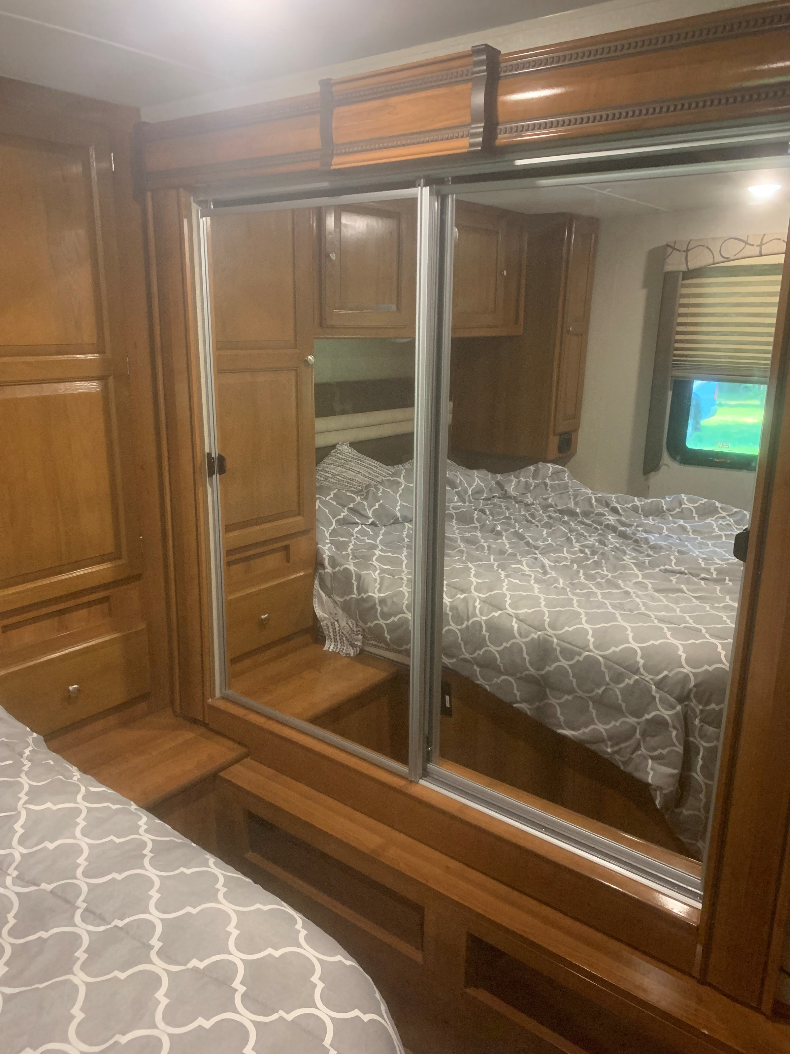 Cozy RV rental bedroom with a mirrored closet, wood interior, and comfy bed, reflecting the sleeping area and window.. Forest River Coachmen Leprechaun 2018