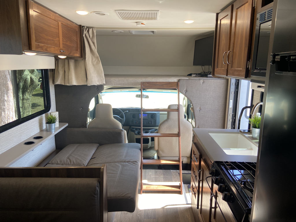 RV rental interior view: compact kitchen, convertible dinette/bed, overhead bunk, and storage for travel.. Winnebago Outlook 2020