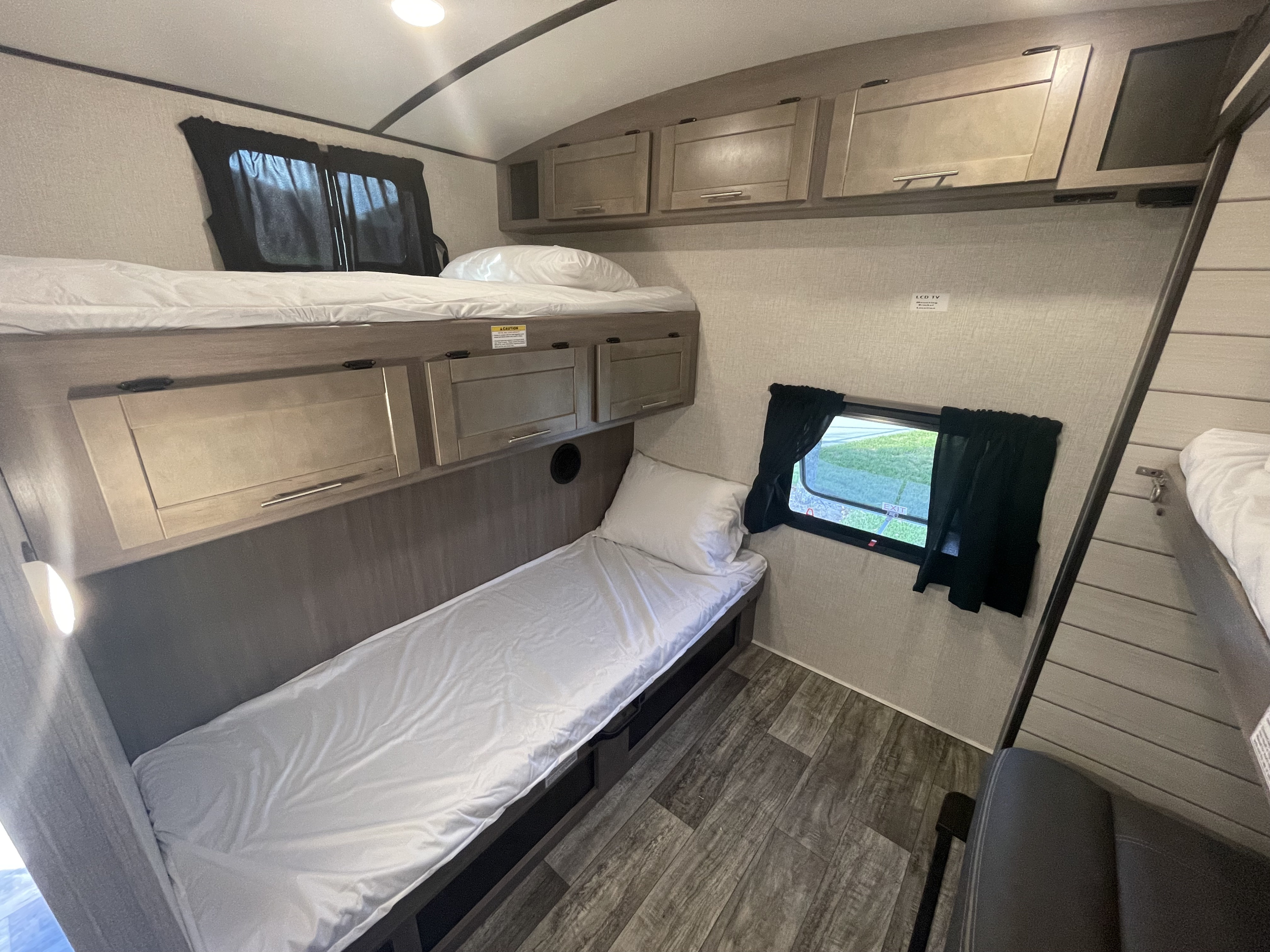 An rv rental's interior featuring two neatly made bunk beds, overhead cabinets, and a window with black curtains.. Crossroads RV Sunset Trail 2022