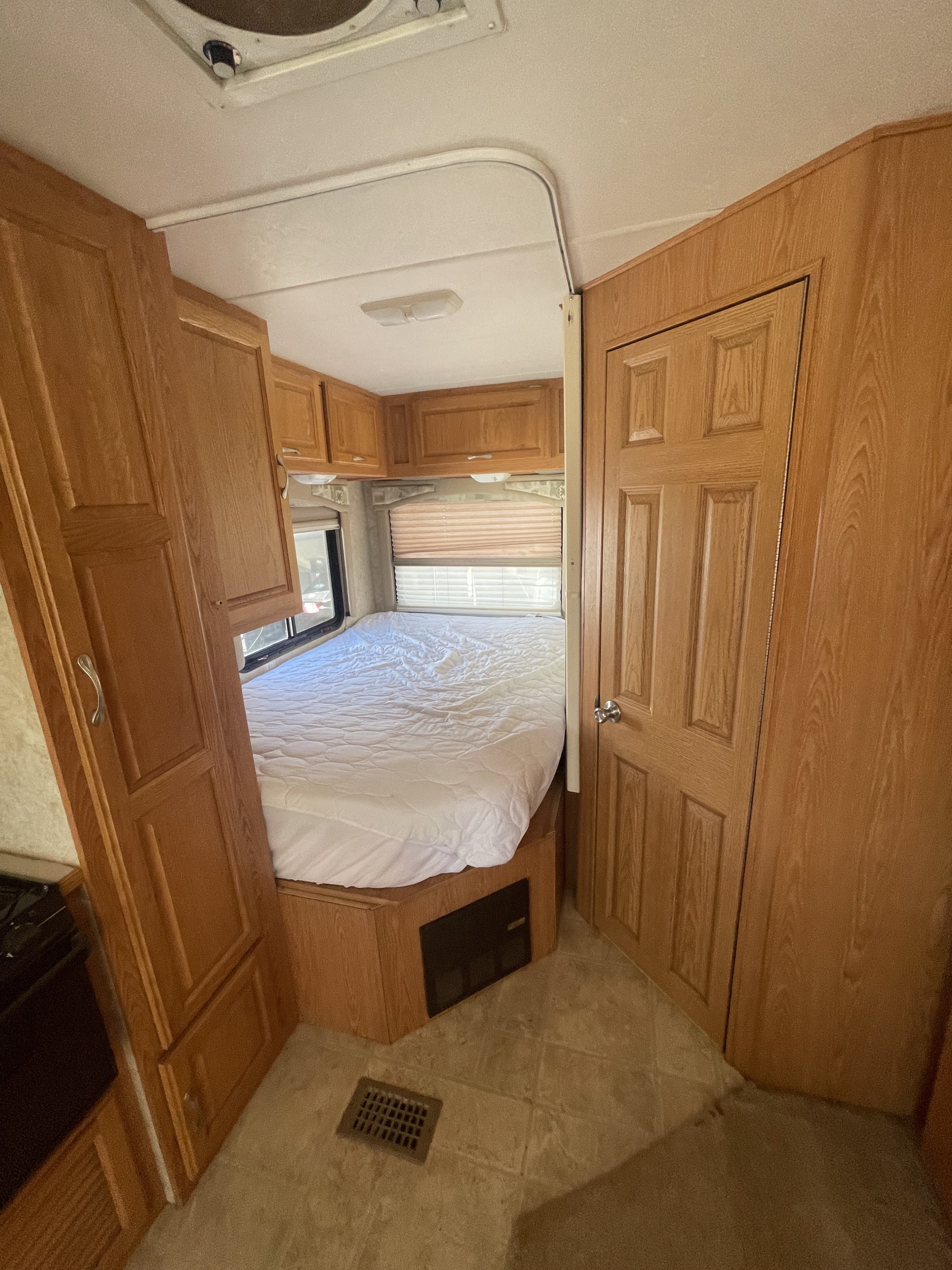 Cozy RV rental bedroom with a comfortable bed, overhead cabinets, and windows. Ideal for travel trailer adventures.. Ford Chateau Sport 2004