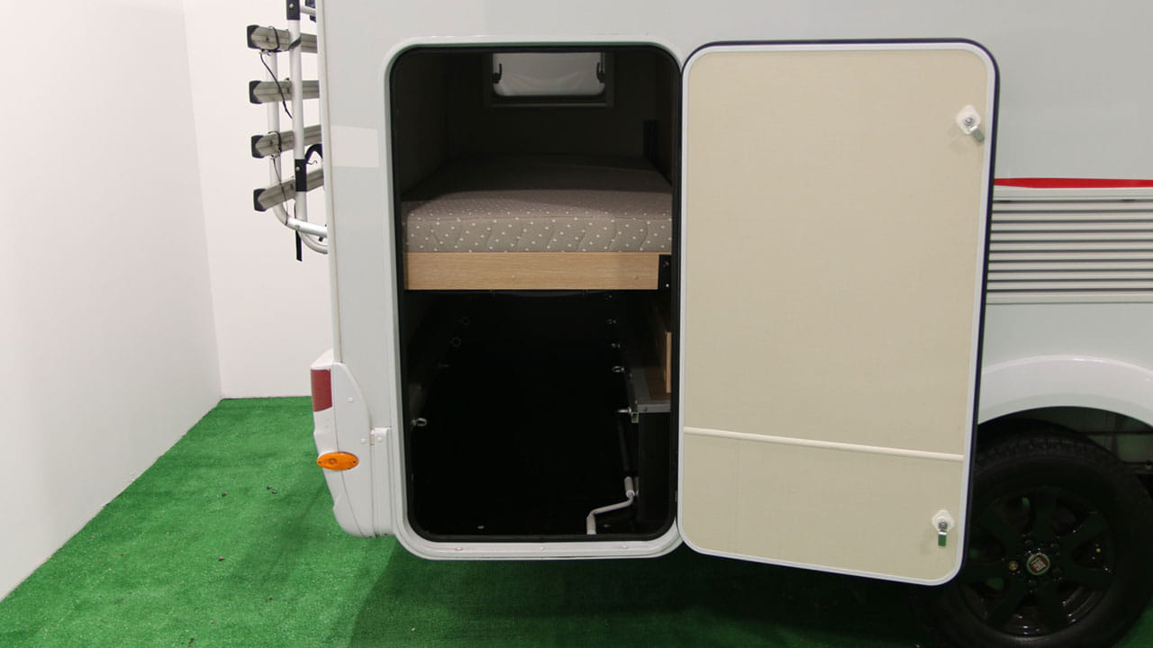 An RV rental's rear is open, showing a bed above a deep storage garage. A bike rack is on the left.. Sunlight A68 2022