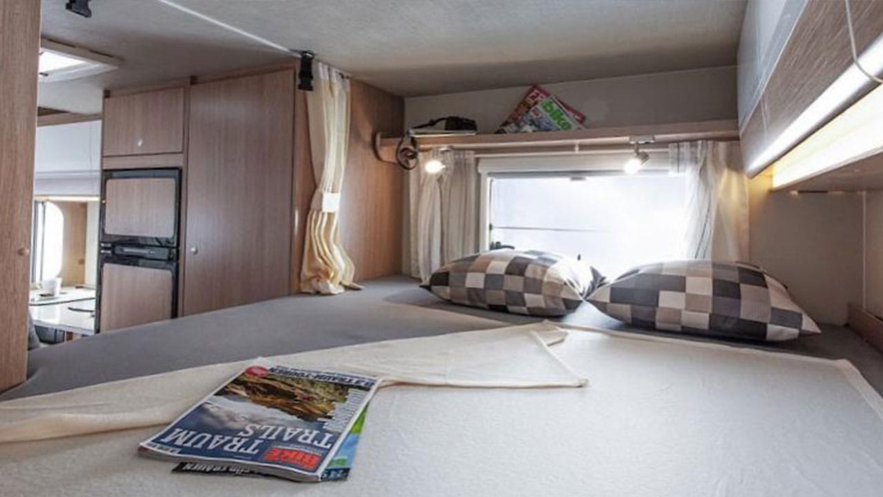 Spacious RV rental interior features a comfortable bed, storage cabinets, and a compact kitchen/dining area.. Sunlight A60 2022