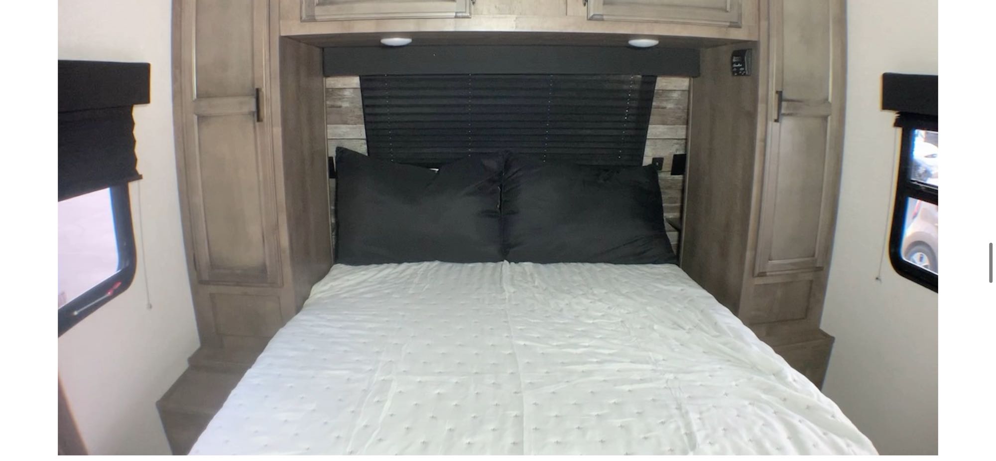 This RV rental bedroom features a comfortable bed with pillows, overhead cabinets, and side windows with blinds, ideal for travel.. Venture Sporttrek 2022