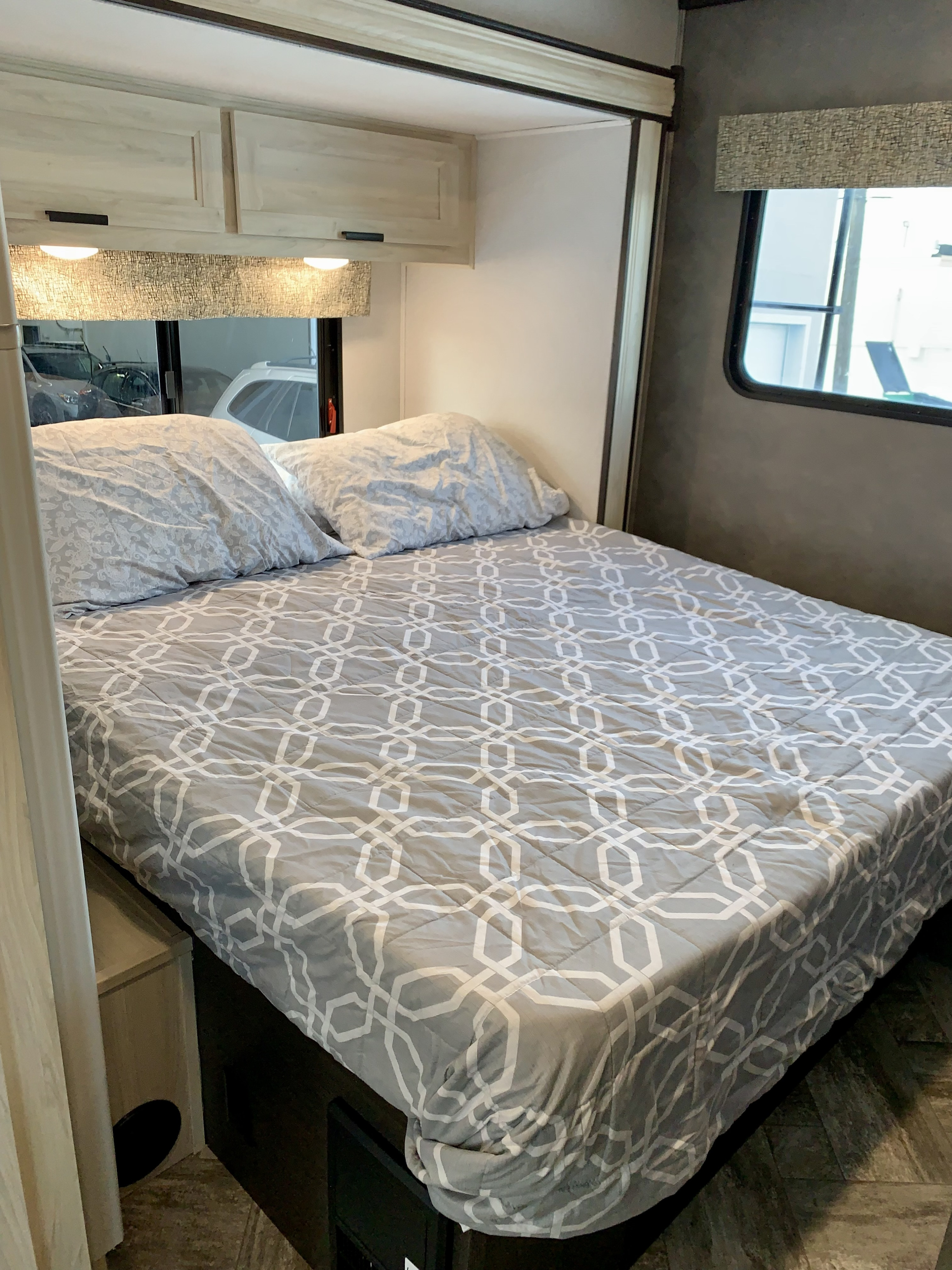 This RV rental bedroom features a comfortable bed with a modern gray geometric comforter, pillows, and overhead cabinets.. Forest River Forester 2551DSLE 2021