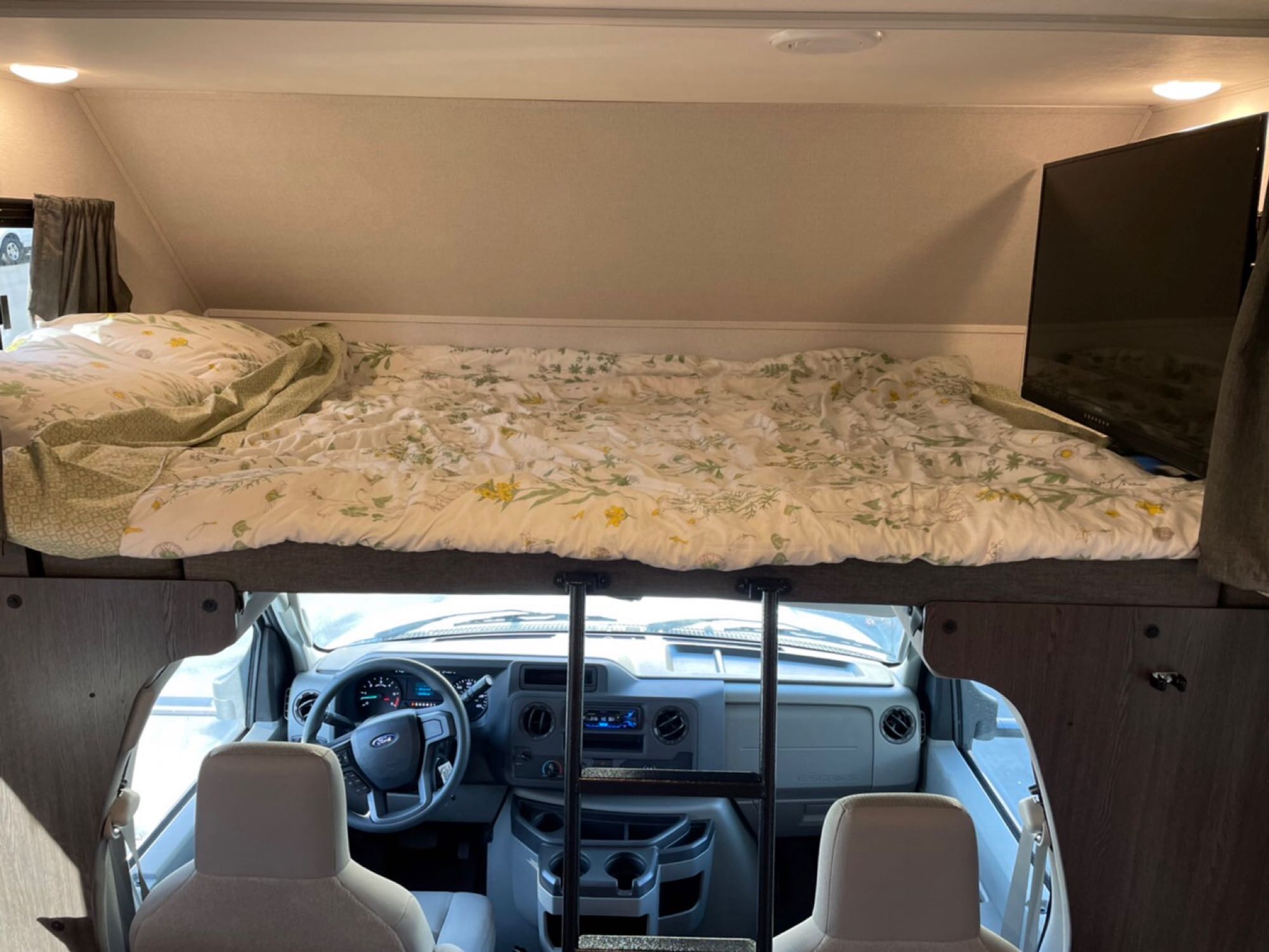 Inside an RV rental: cozy cab-over bunk bed with floral bedding, TV, and view of the driver's area below.. Forest River Other 2022