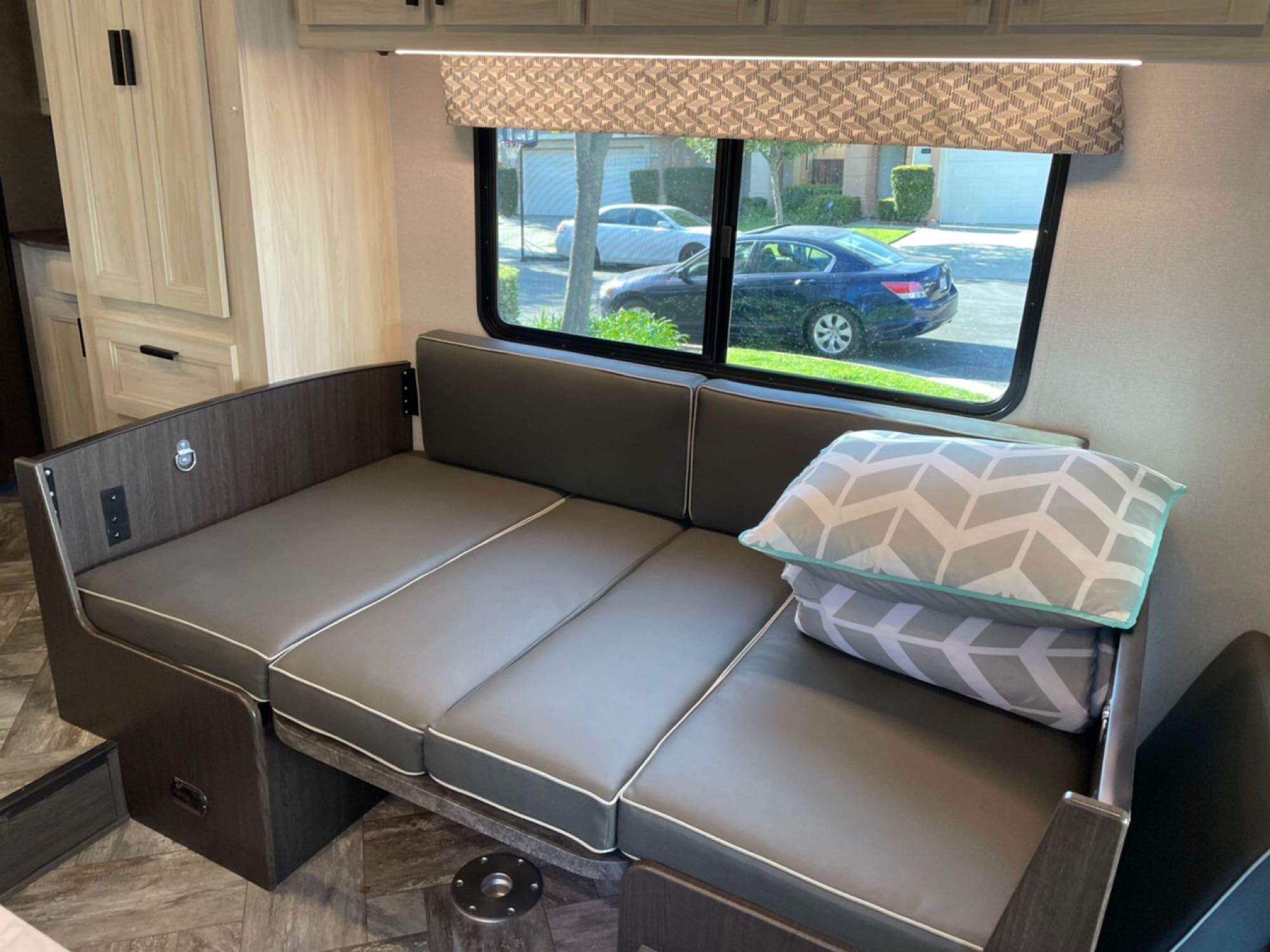Cozy RV rental interior featuring a grey convertible dinette with patterned pillows, light wood cabinets, and a window street view.. Forest River Other 2022