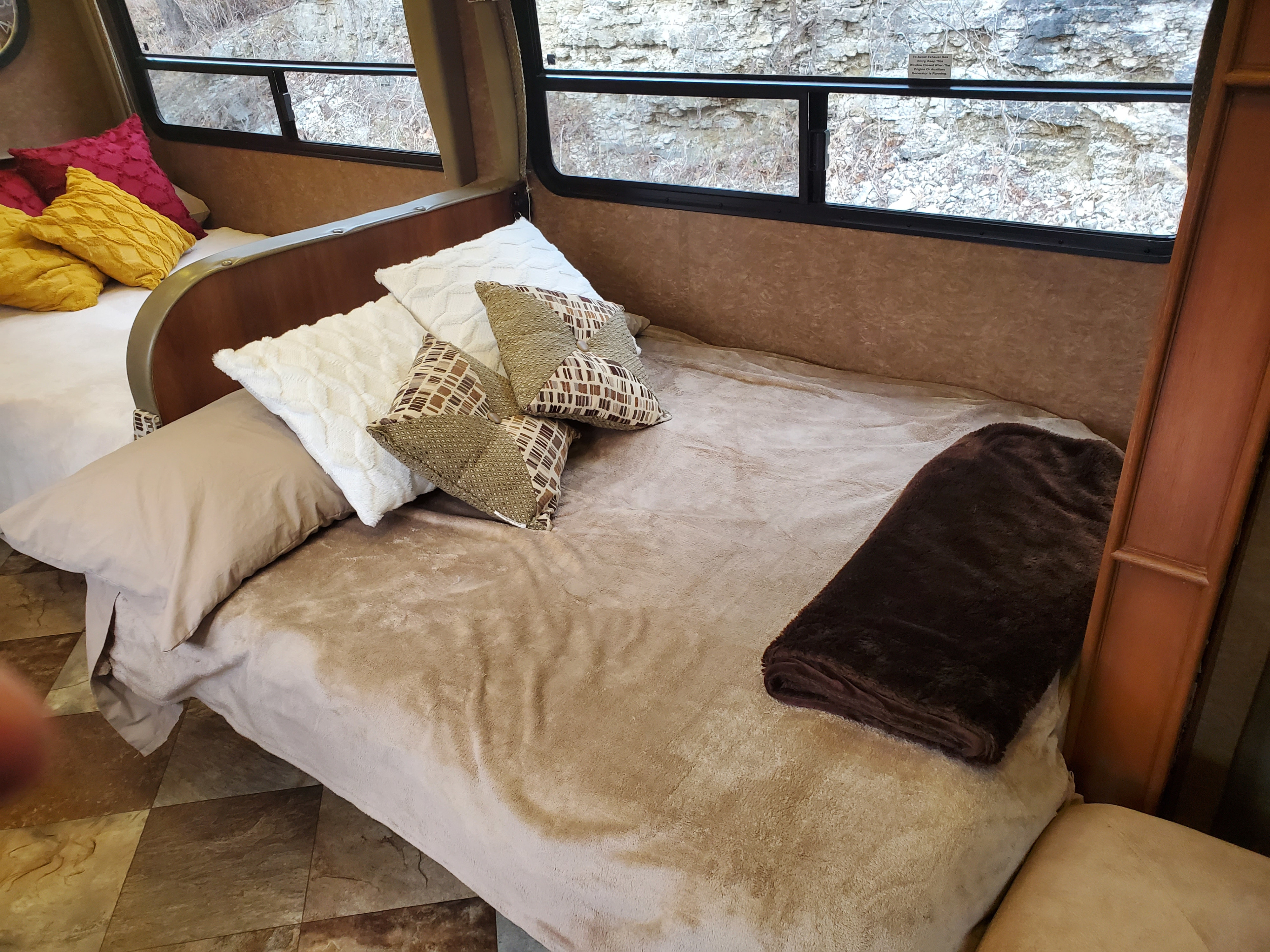Cozy RV rental interior with two beds, colorful and neutral pillows, and large windows showing a rocky outdoor view.. Forest River Coachmen Concord 2014