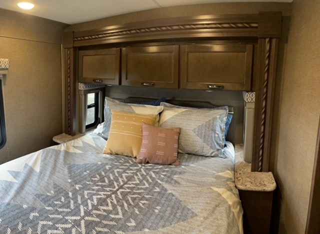 An inviting RV rental bedroom with modern decor, a large bed, overhead storage, and side tables for your travel comfort.. Thor Freedom Elite 2018